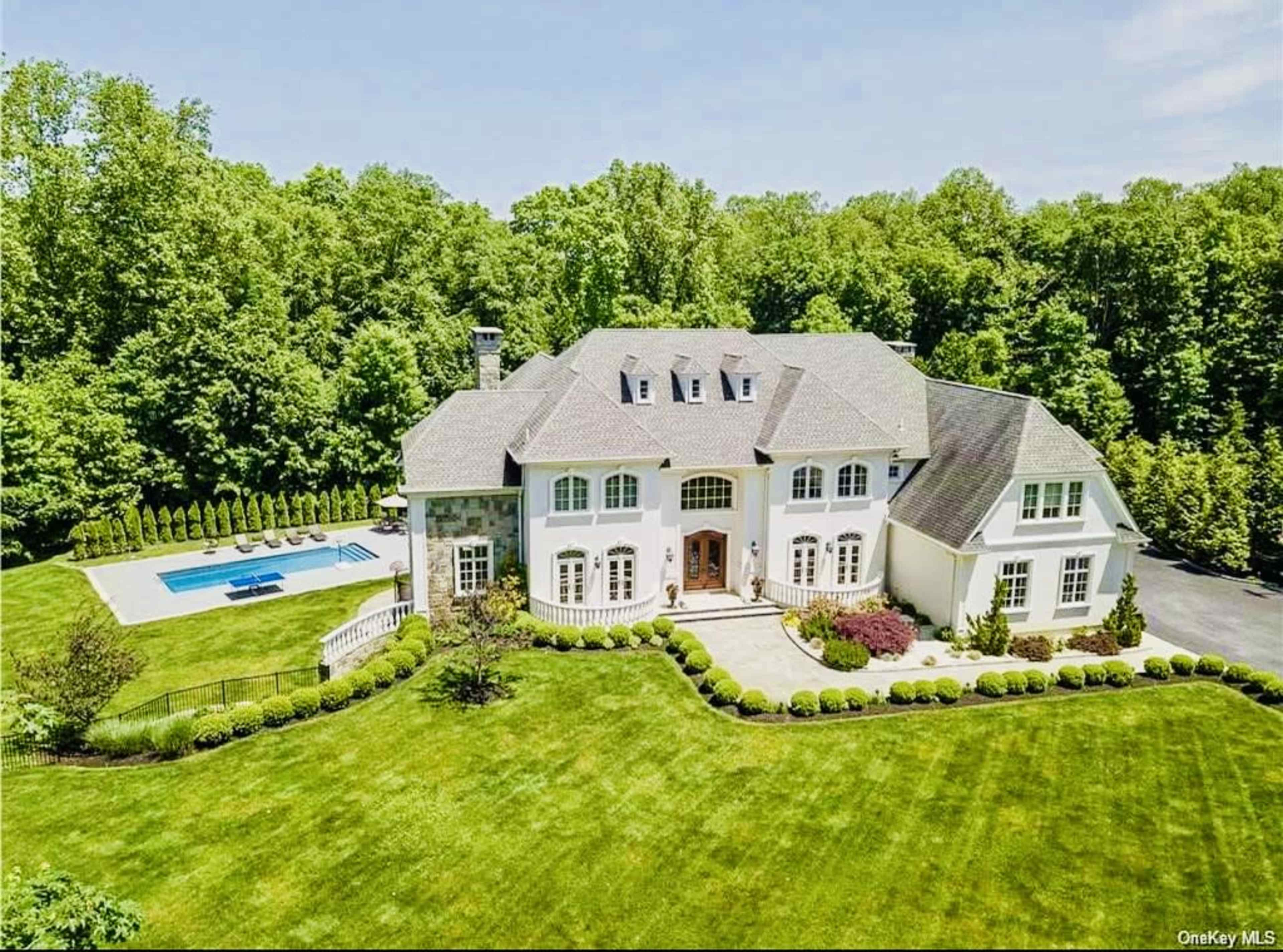 The image shows a large, elegant house surrounded by manicured lawns and a swimming pool in the backyard.