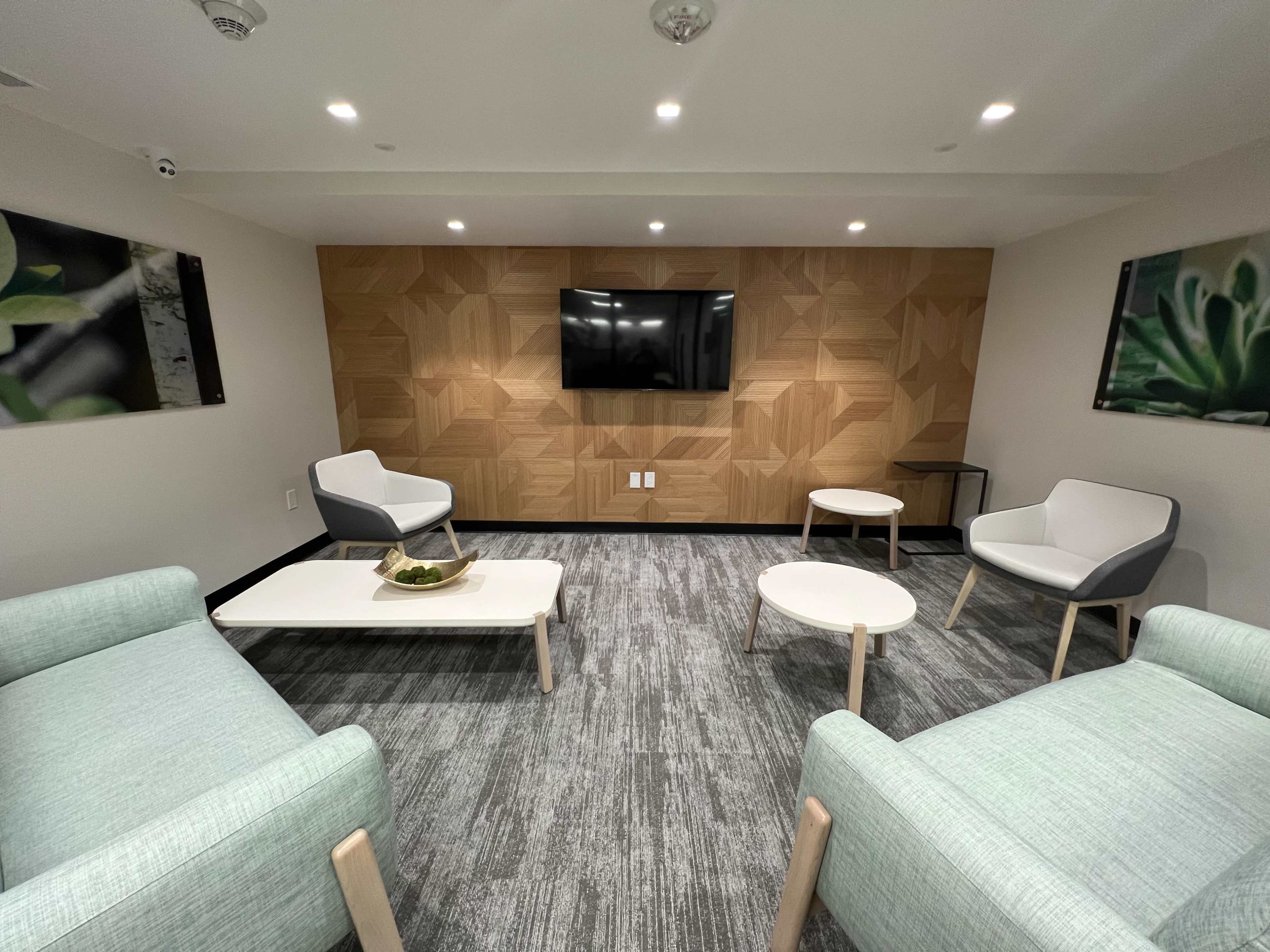 A modern lounge area with light green upholstered chairs, a white coffee table, and a wooden feature wall with a TV.