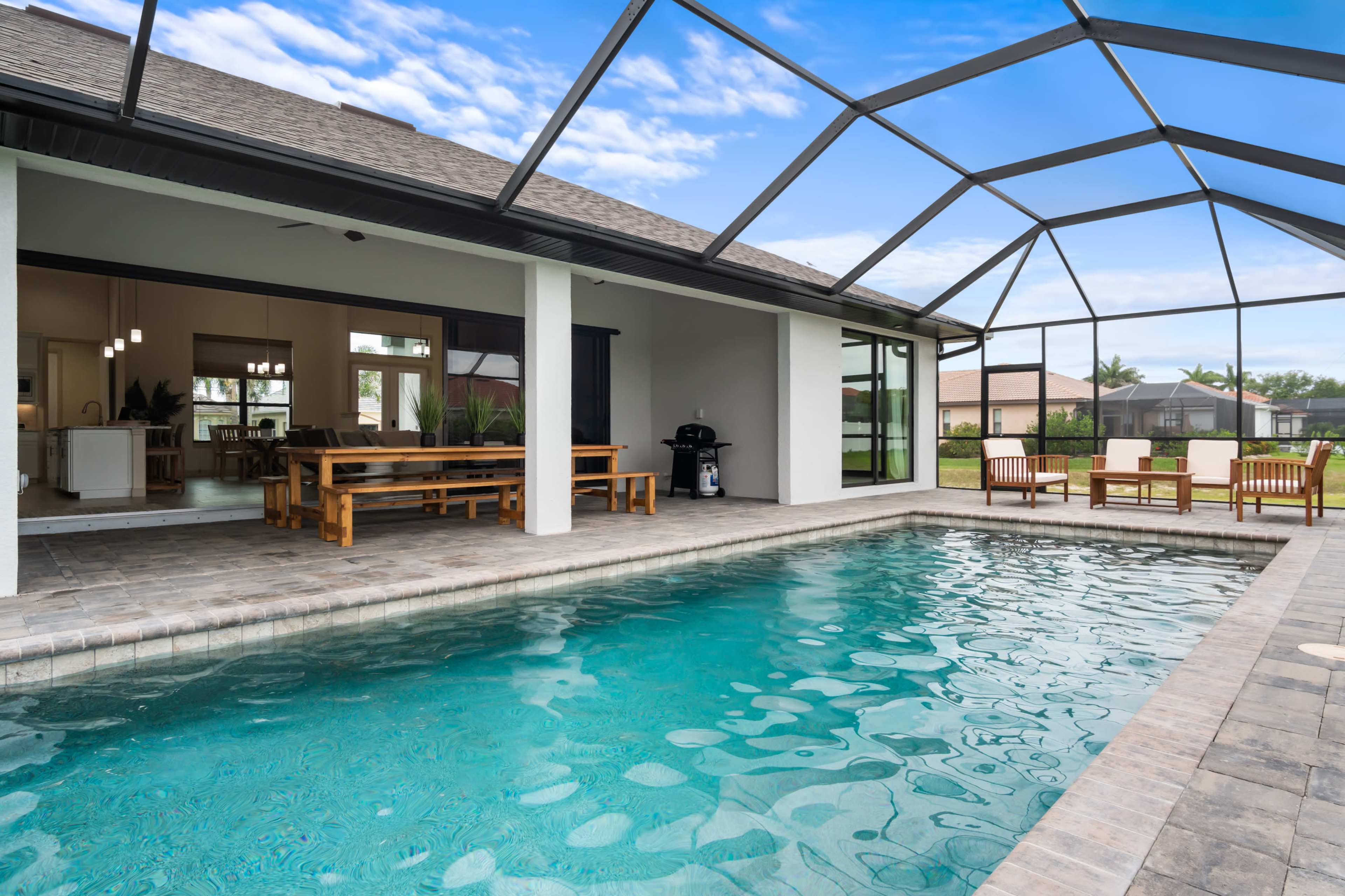 A backyard pool surrounded by a screened enclosure, with seating areas and visible access to an adjacent indoor dining space.