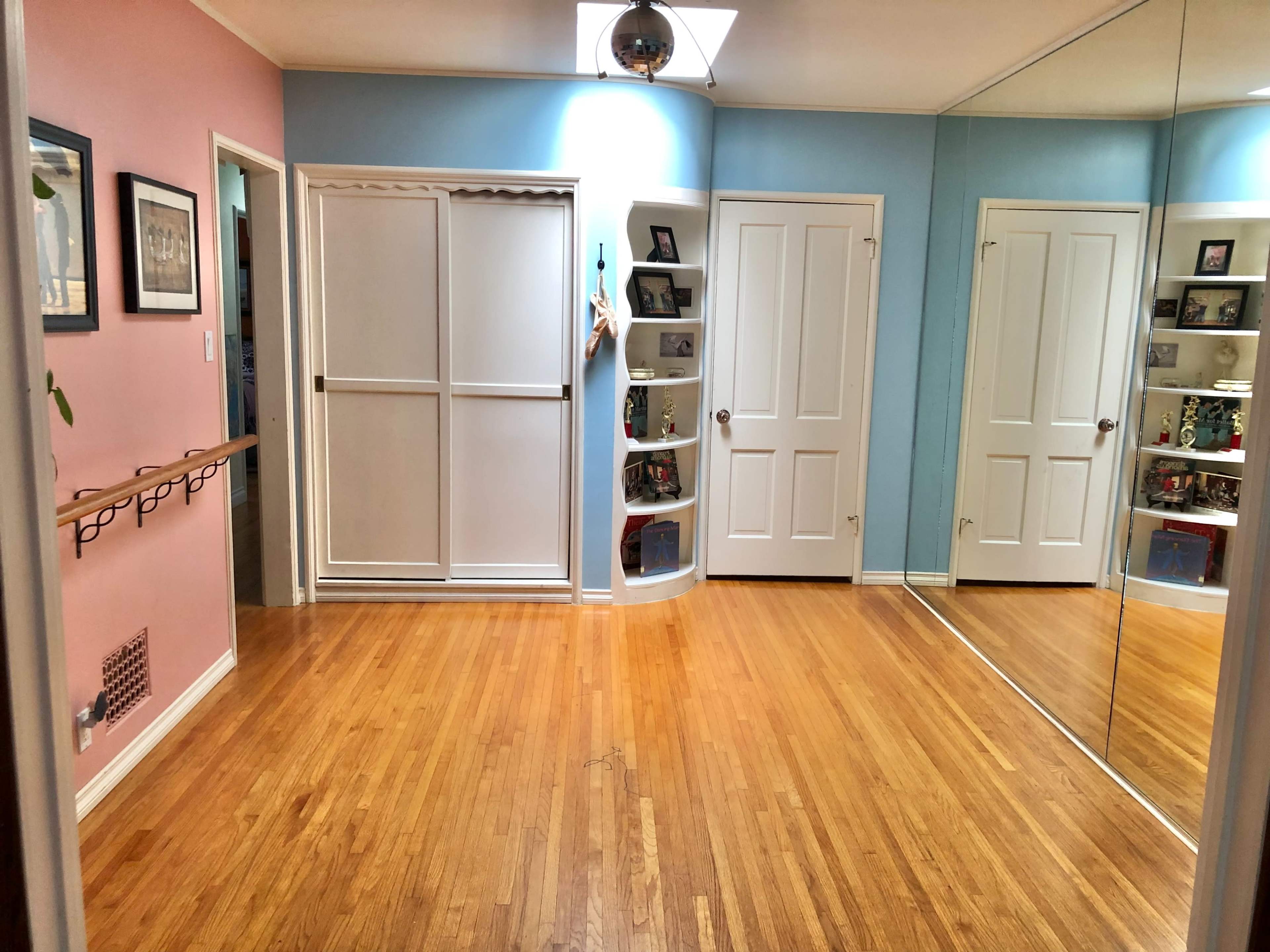 The image shows a room with hardwood floors, pale pink and blue walls, and mirrored closet doors.