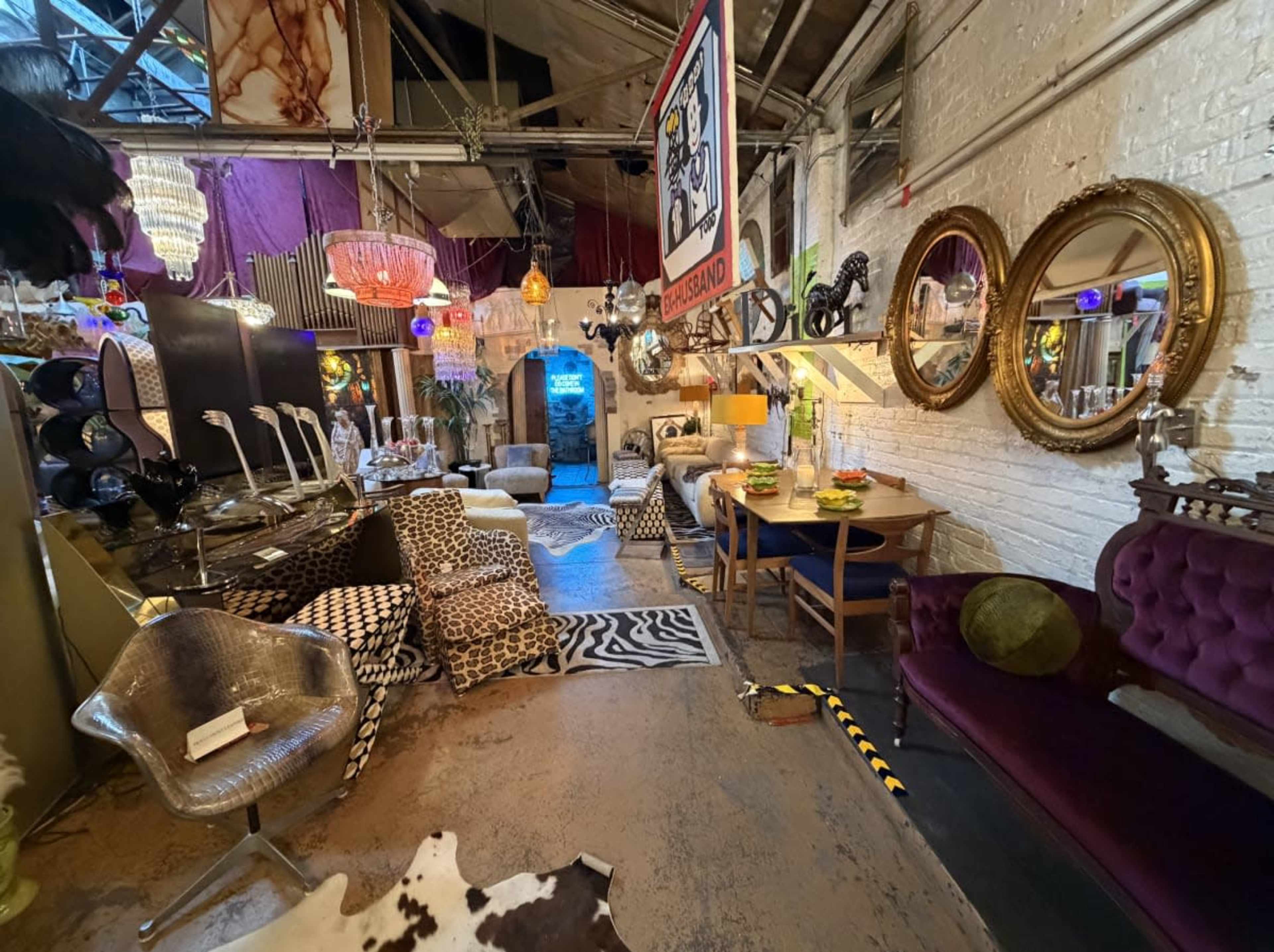 The image shows a vibrant interior space filled with eclectic furniture, decorative items, and various lighting fixtures.