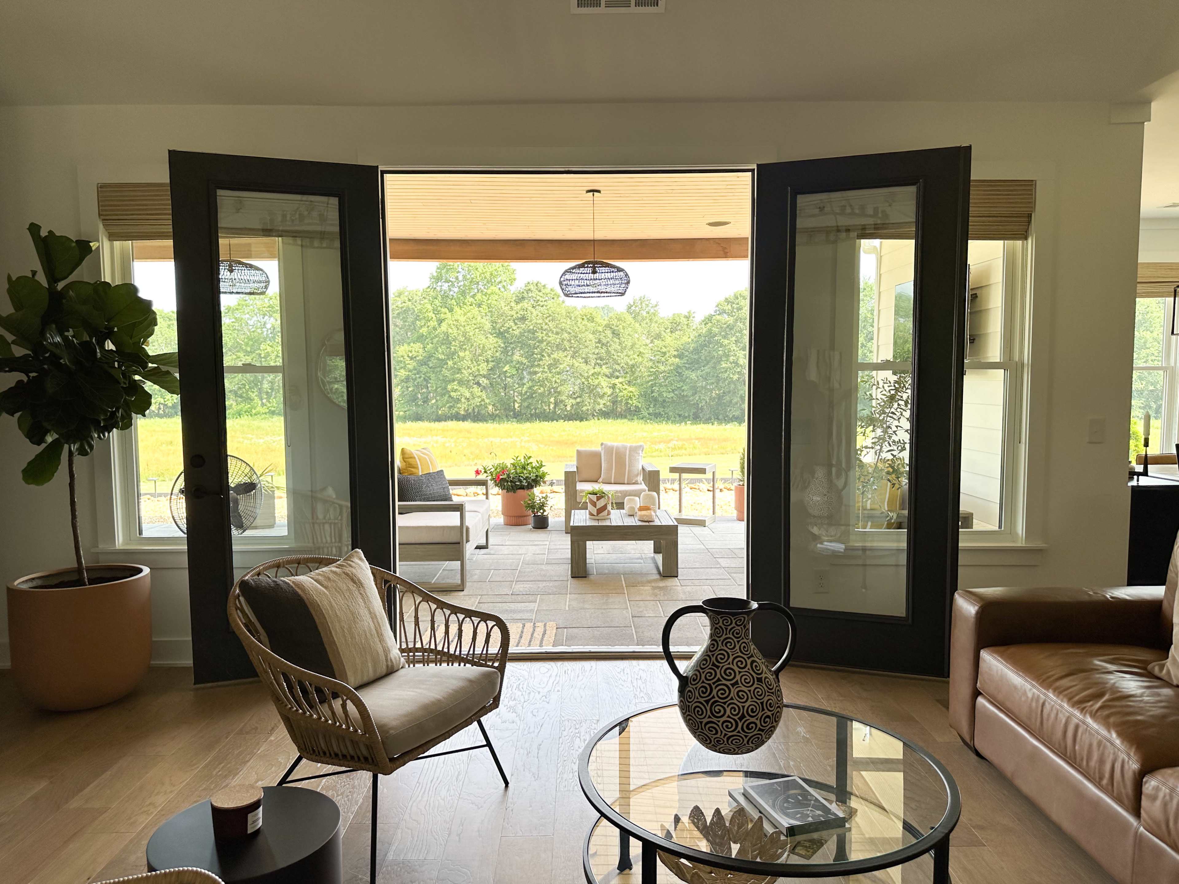 A living room with open double doors leading to a patio area surrounded by greenery.