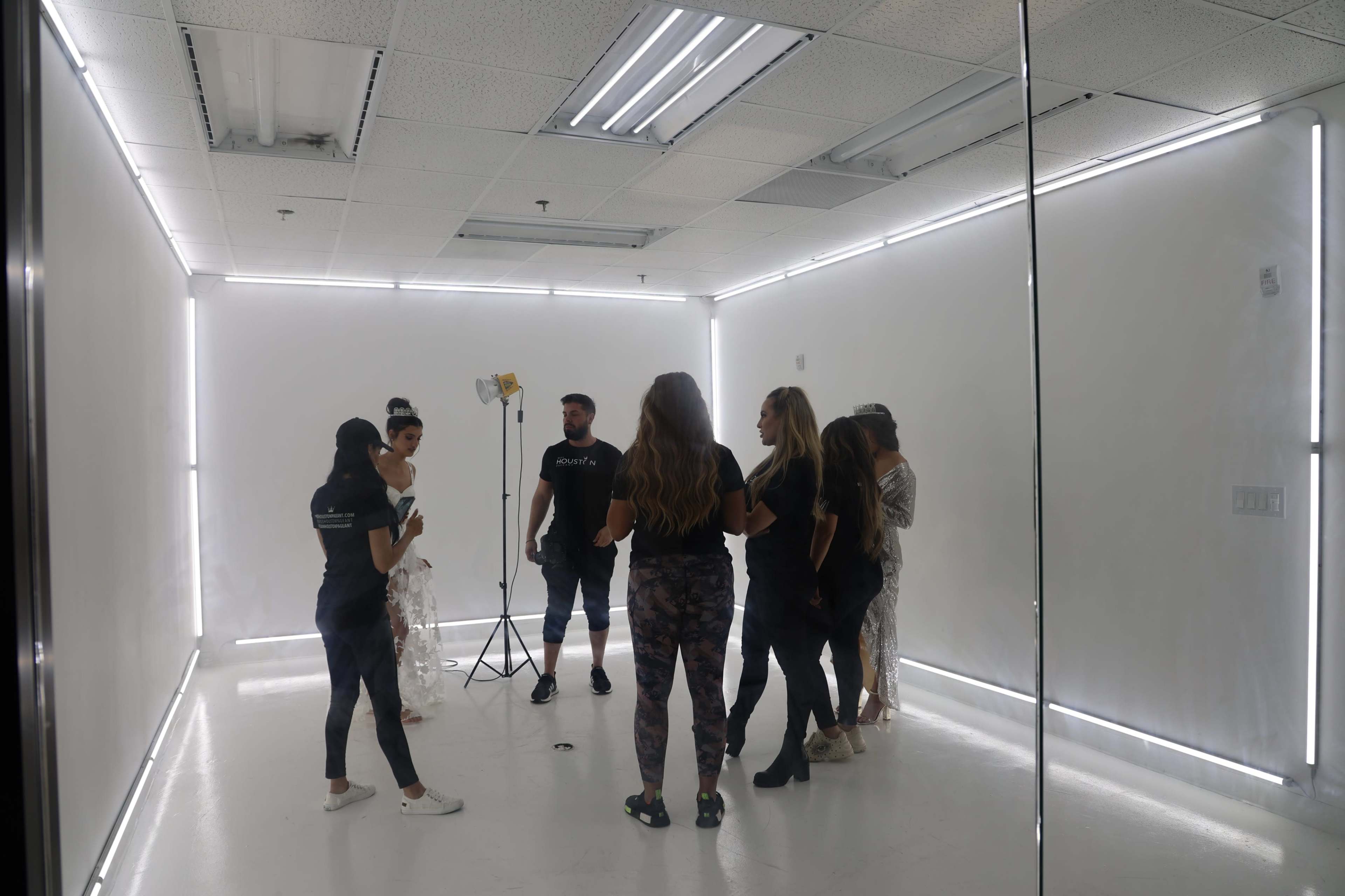 A group of seven people stands together in a brightly lit, minimalistic studio space with white walls and ceiling lights.