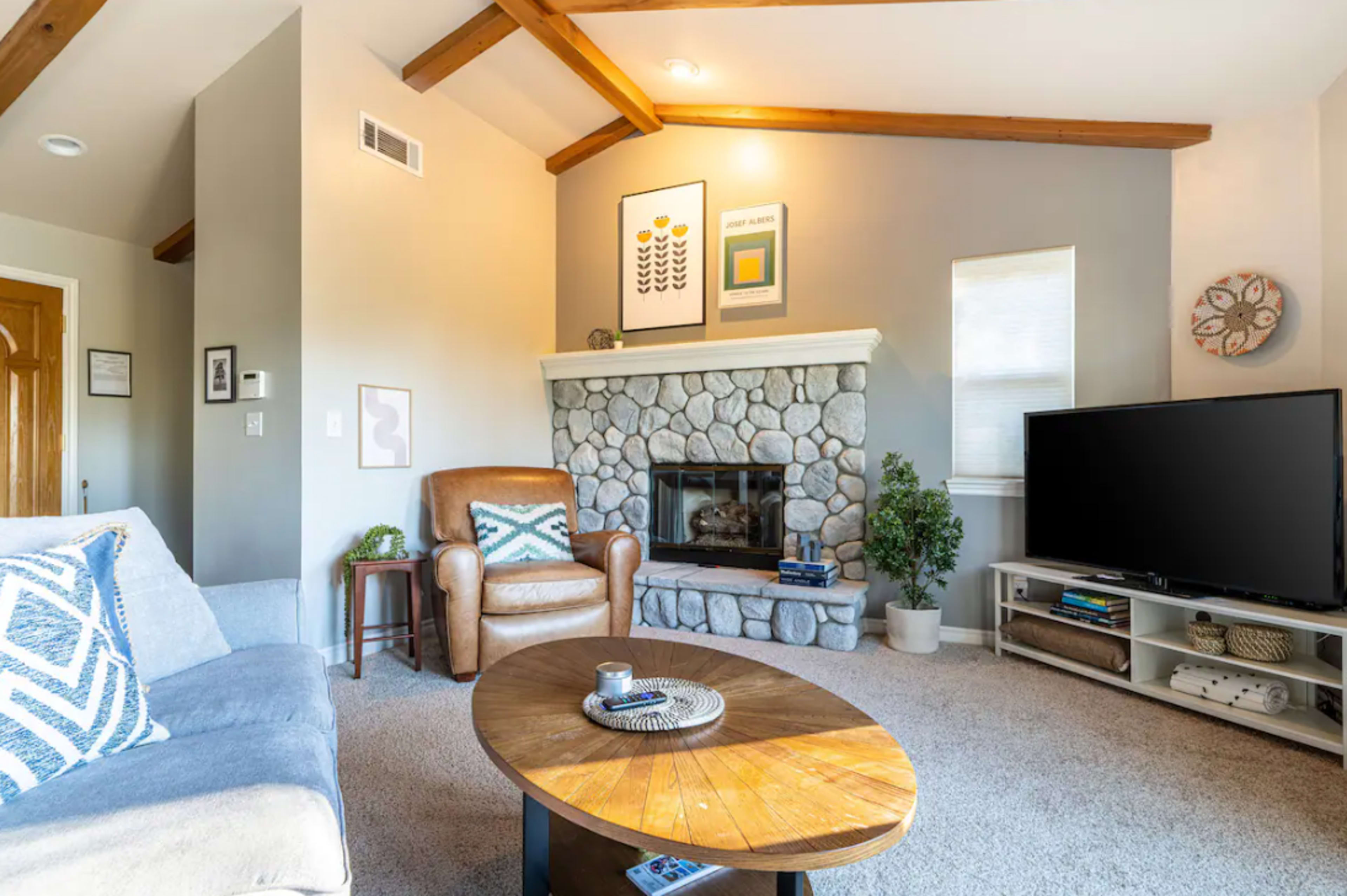The living room features a stone fireplace, a comfortable seating area, and a television unit against a light-colored wall.