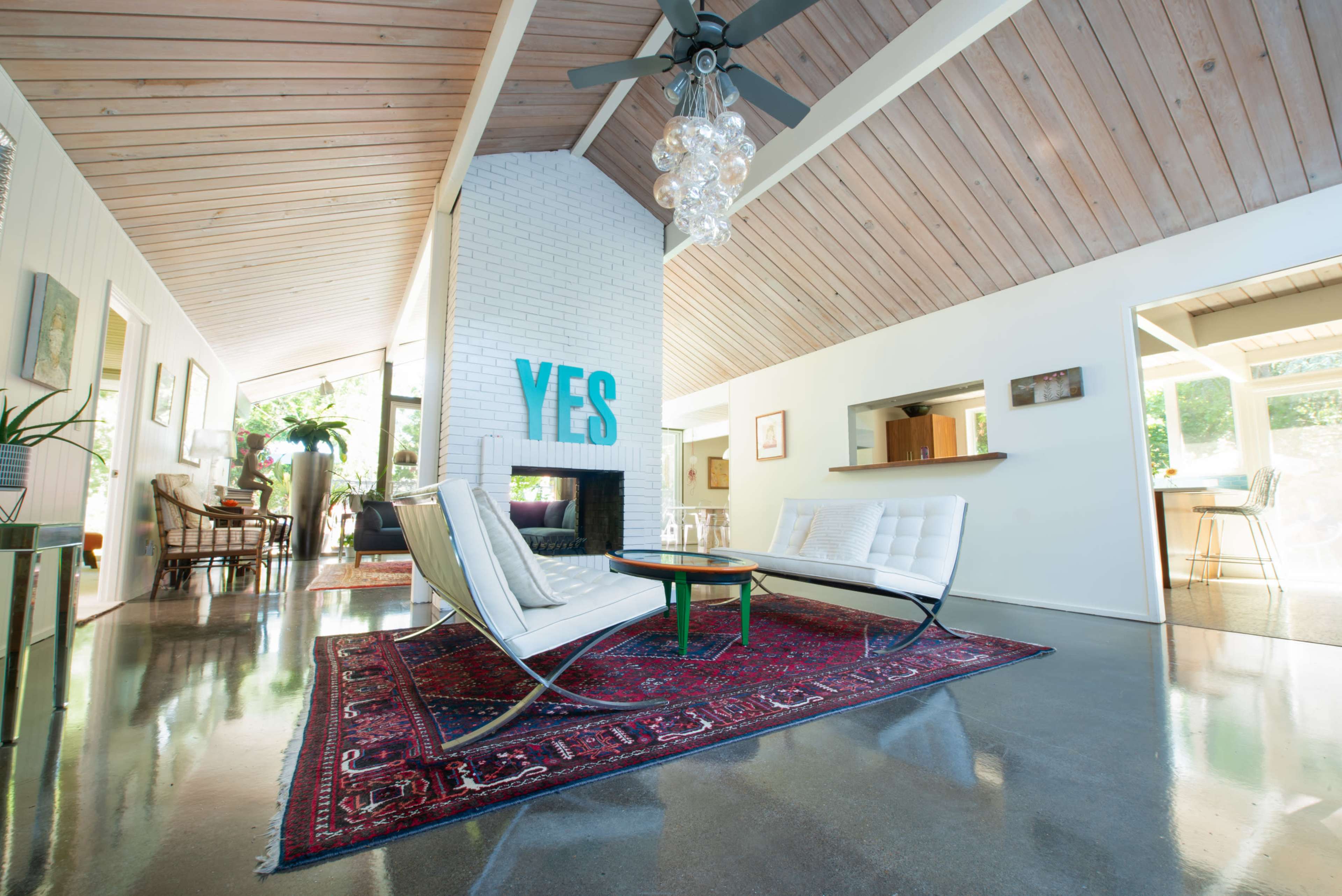 A spacious living room features a white leather sofa, a glass coffee table on a patterned rug, and a decorative wall with the word "YES" displayed.