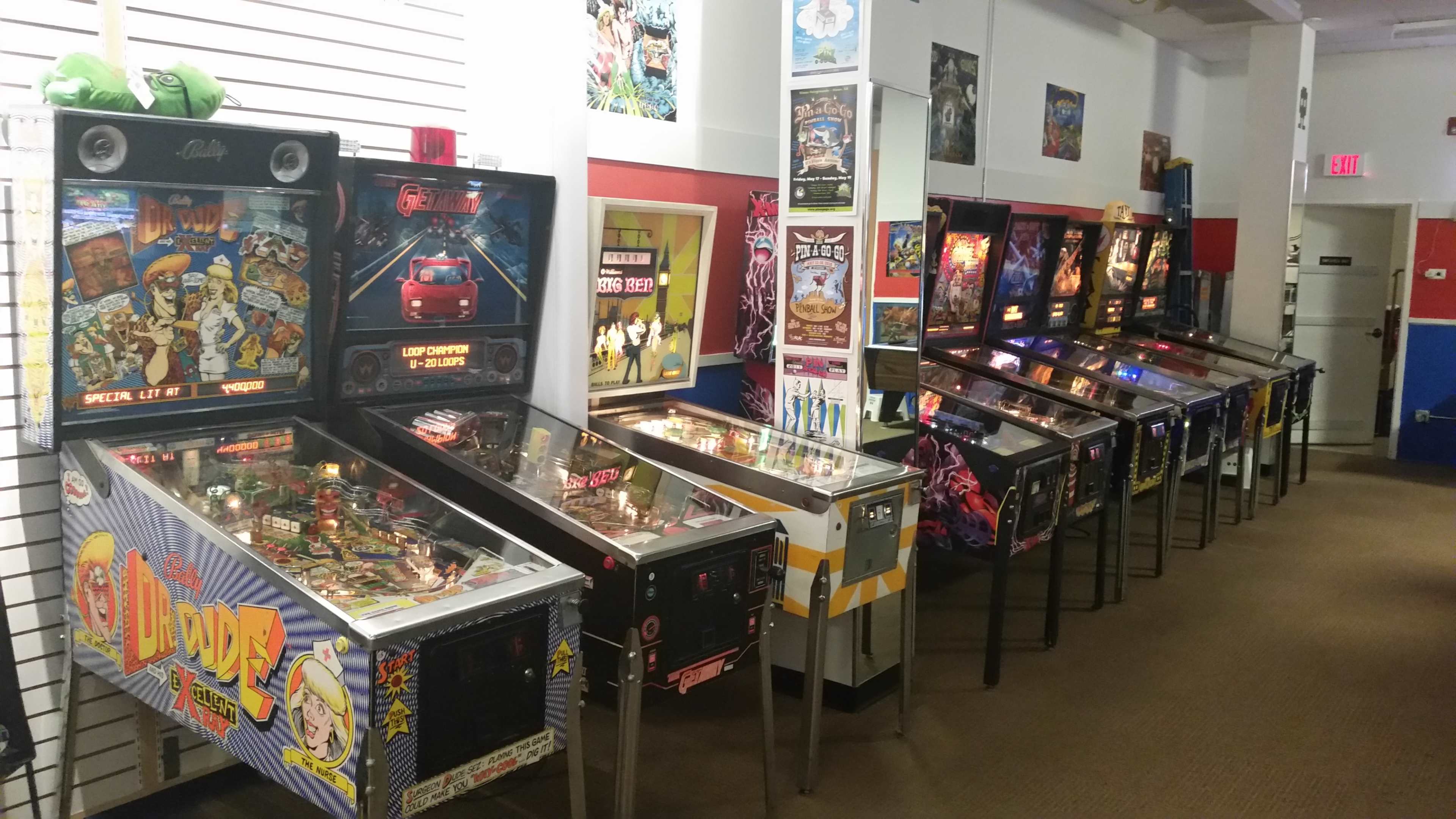 The image shows a row of pinball machines lined up against the wall in a game room, featuring various colorful designs and themes.