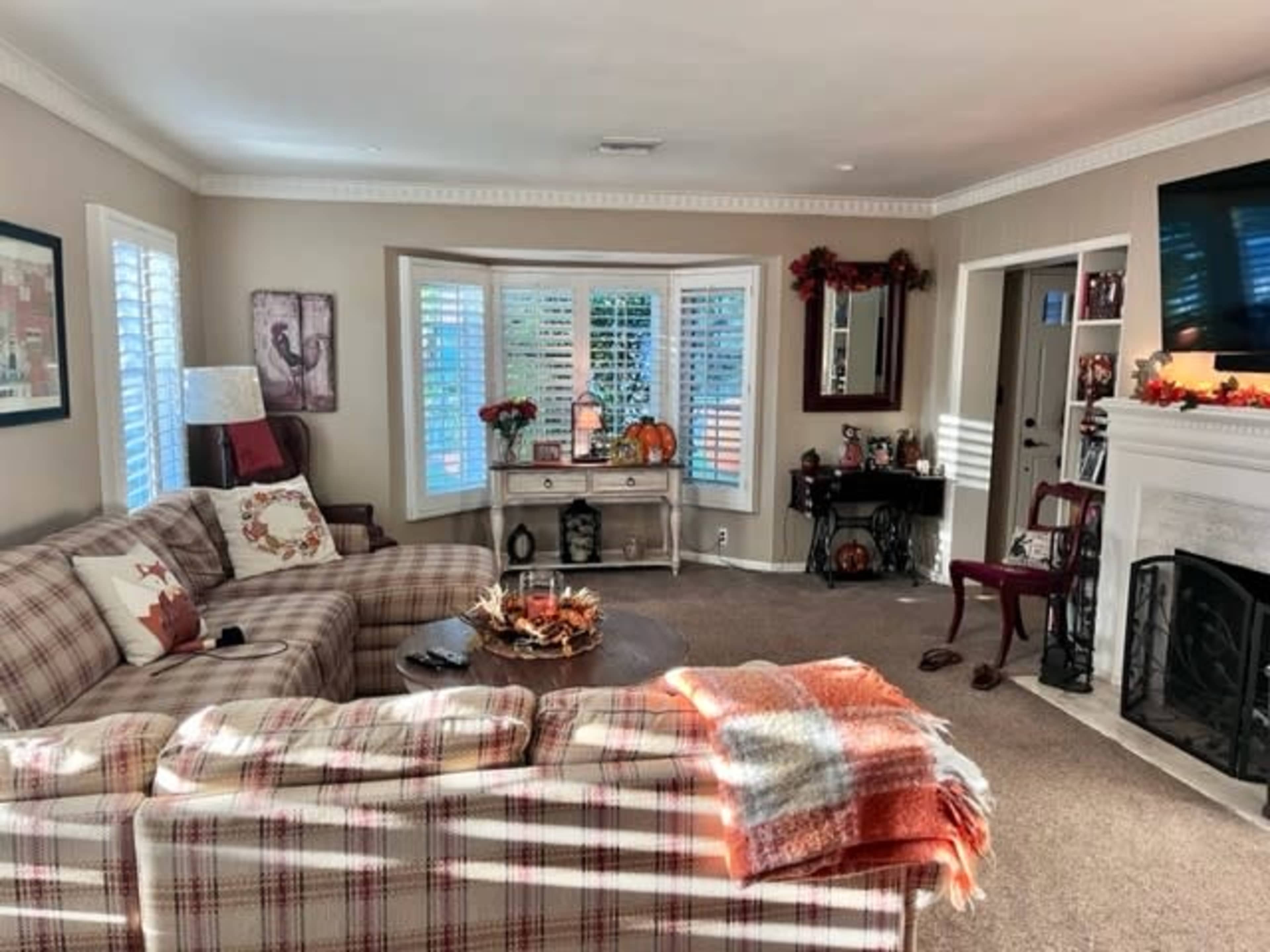 A cozy living room featuring a plaid sectional sofa, a decorative coffee table, and a fireplace surrounded by seasonal decorations.