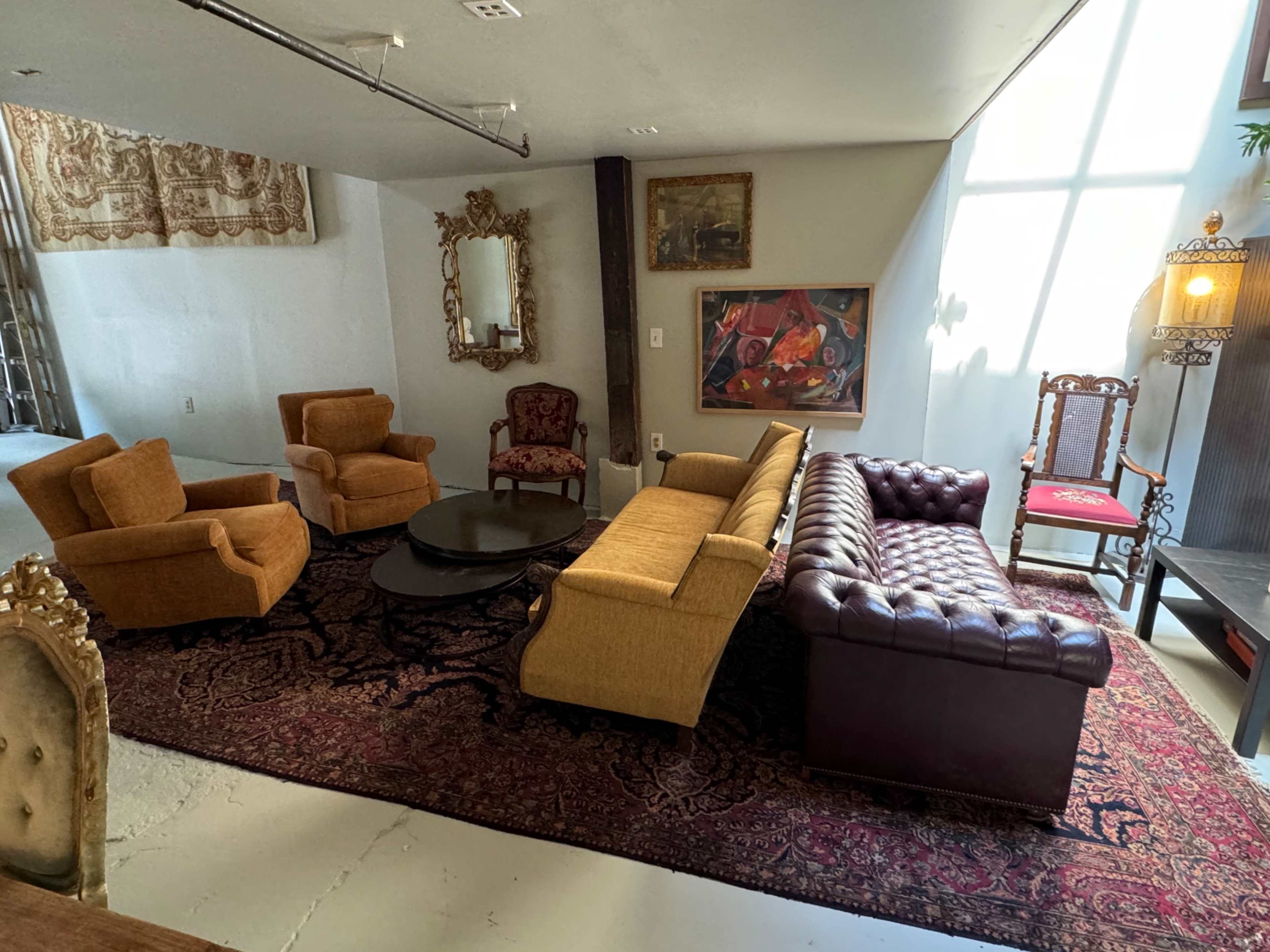 A living area with a mix of upholstered seating, a round coffee table, and a large patterned rug.