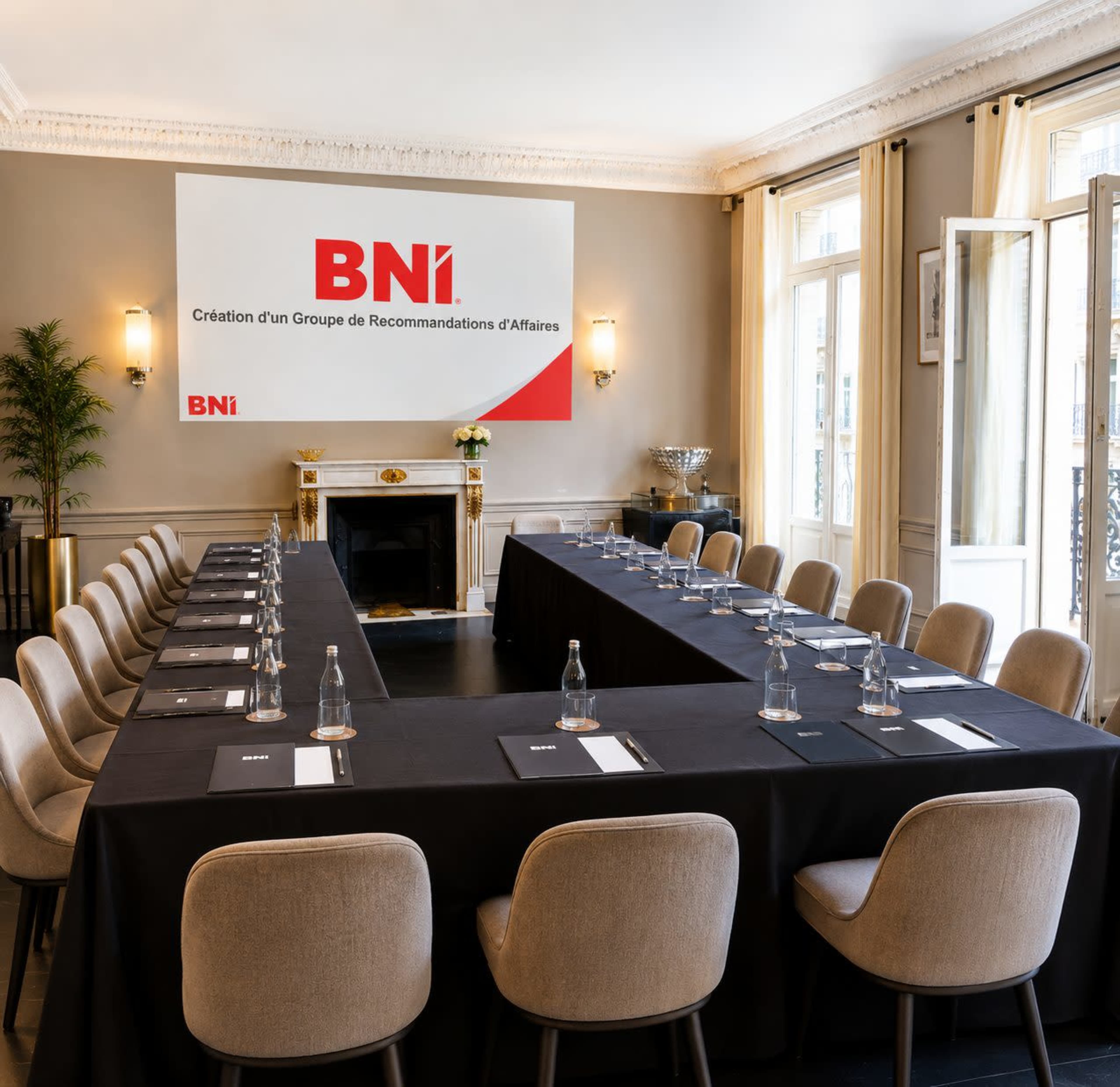 The image shows a neatly arranged conference room with a long table set for a meeting, featuring chairs and a banner displaying the BNI logo on the wall.