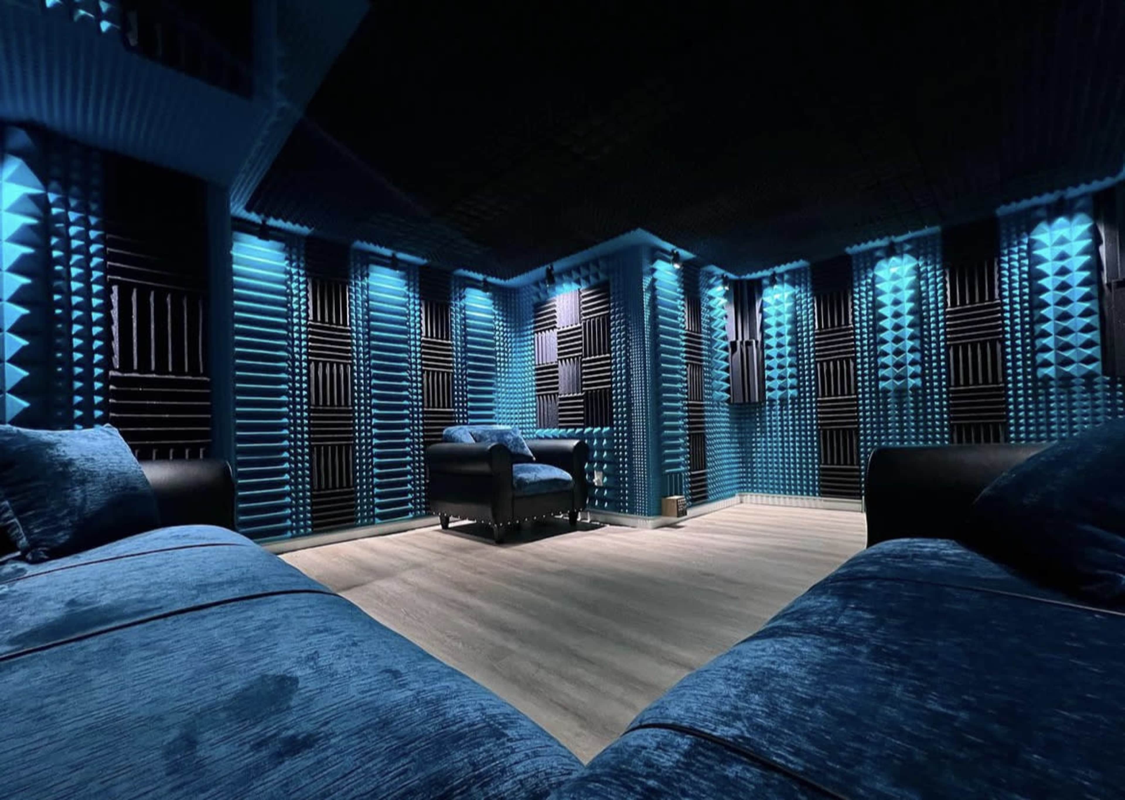 A soundproof room with blue lighting, featuring foam acoustic panels on the walls and a dark blue couch.