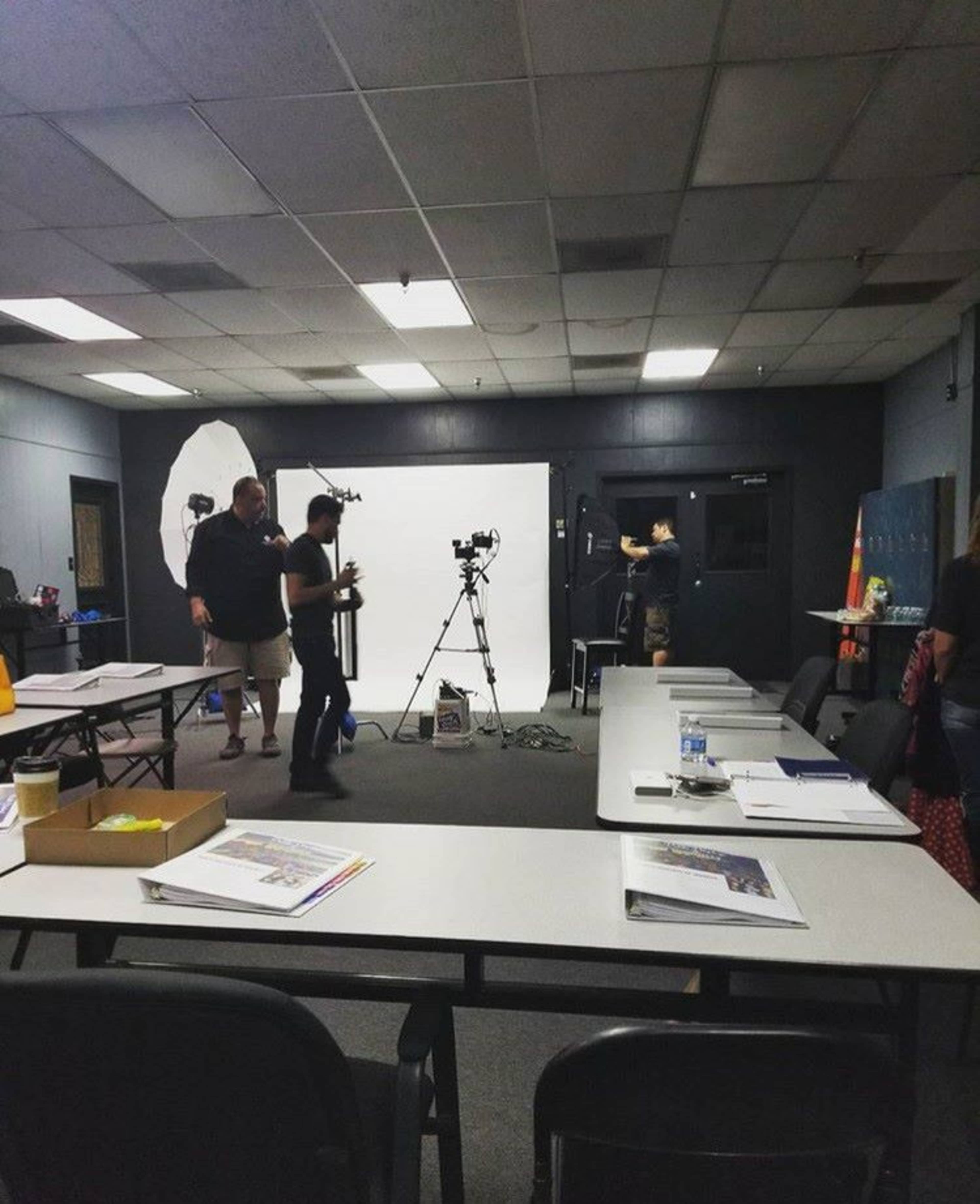 A group of people is setting up a photography studio in a room with a backdrop and lighting equipment.