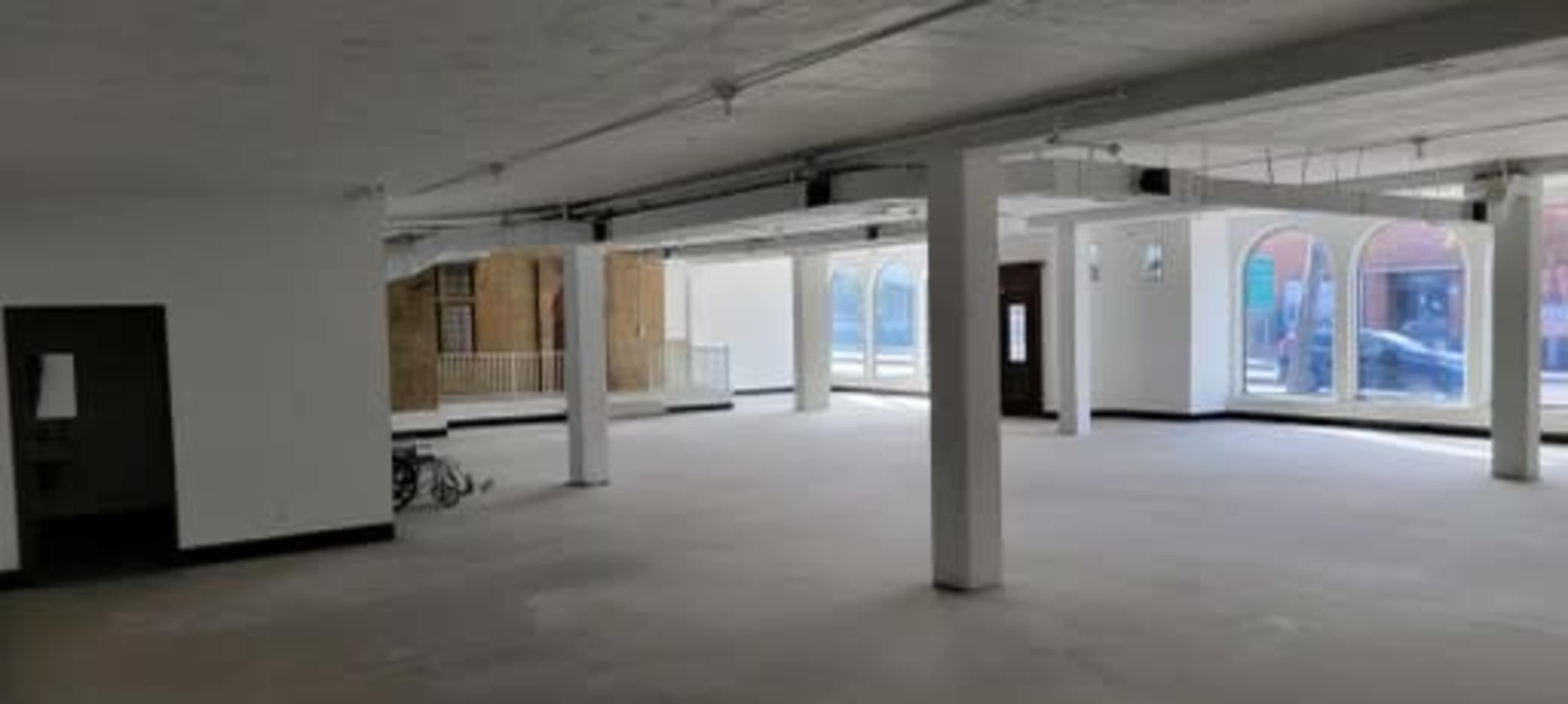 A large, empty interior space with white walls, exposed columns, and large windows.