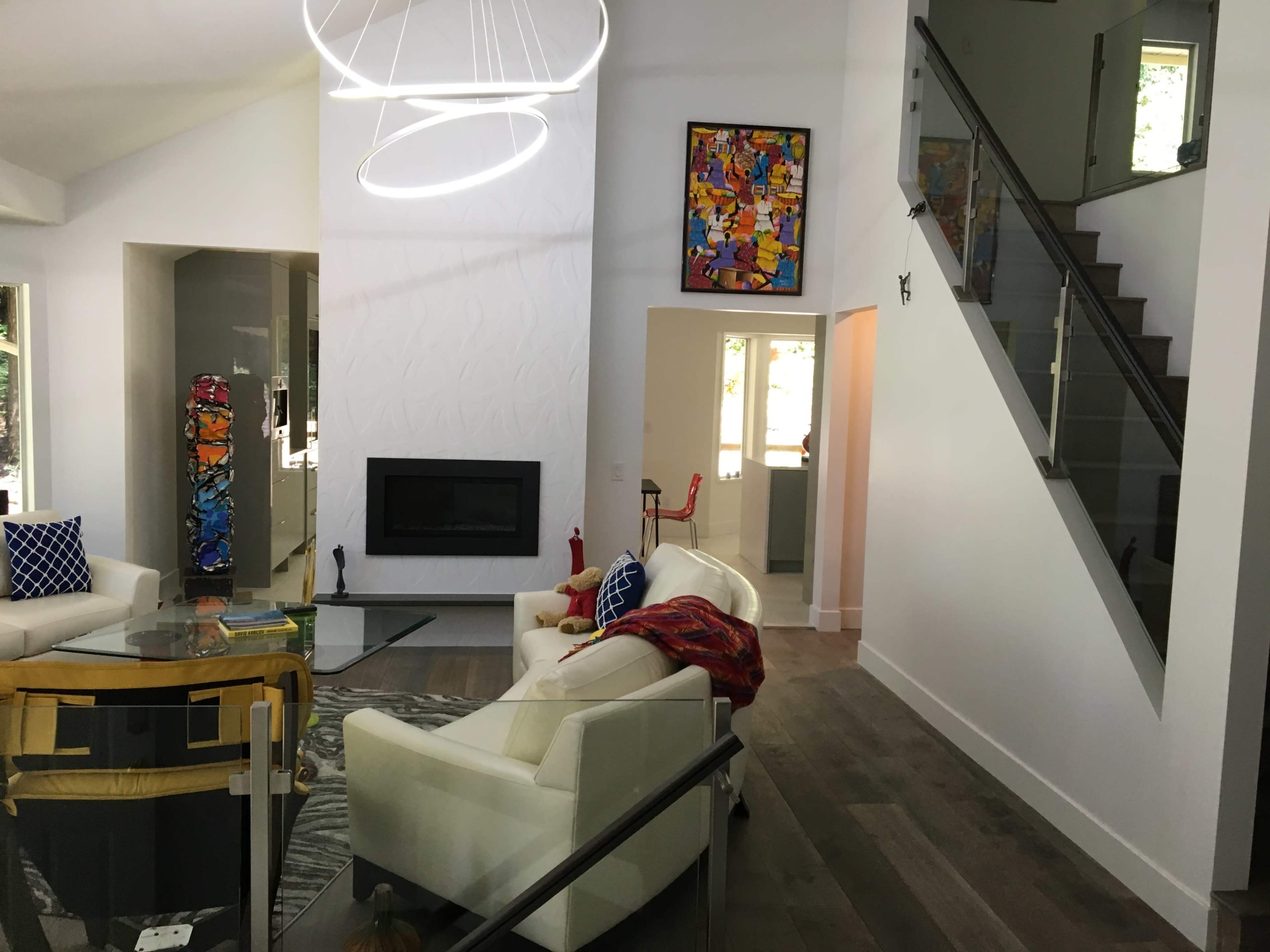 A modern living space featuring a glass staircase, a fireplace, a colorful piece of artwork on the wall, and contemporary furniture.