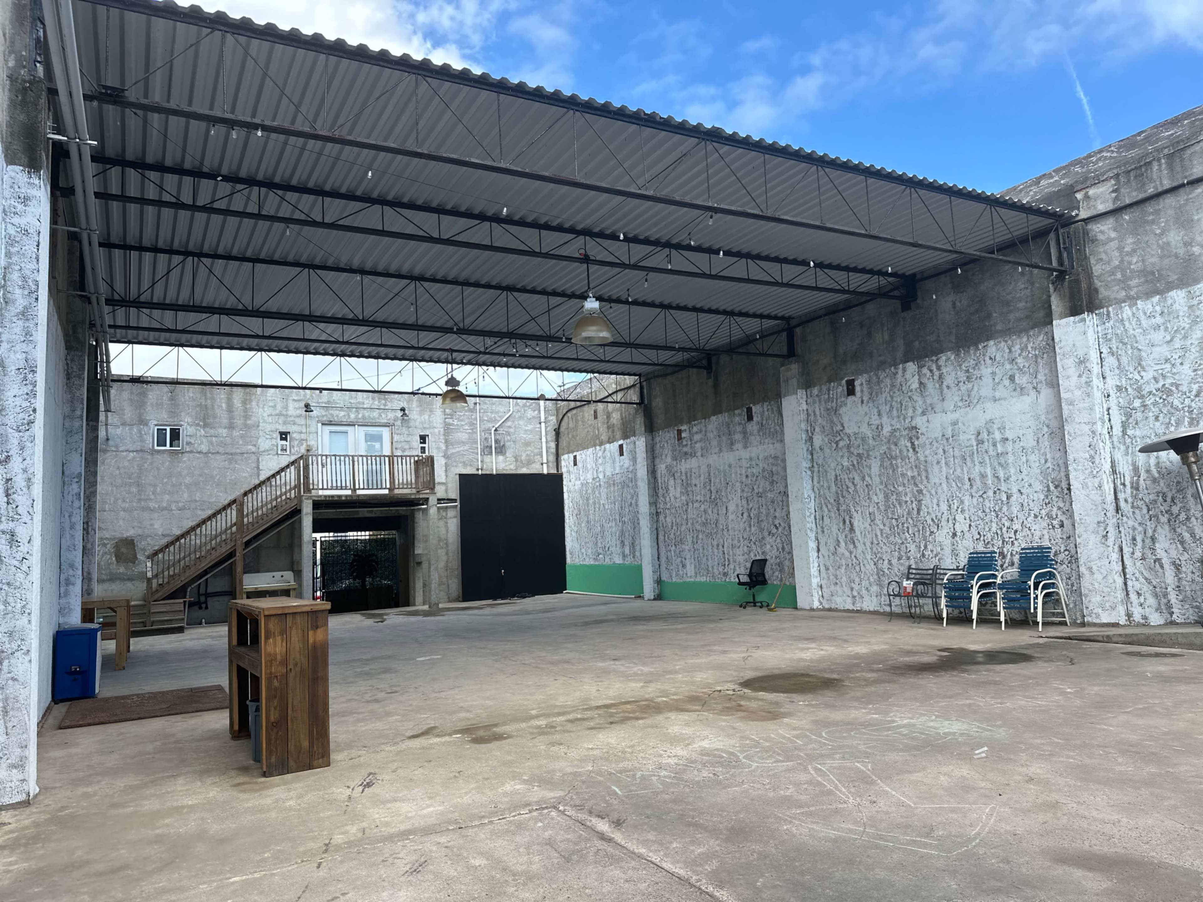 The image shows an open, empty warehouse space with a high ceiling, concrete floor, and walls featuring a peeling paint finish.