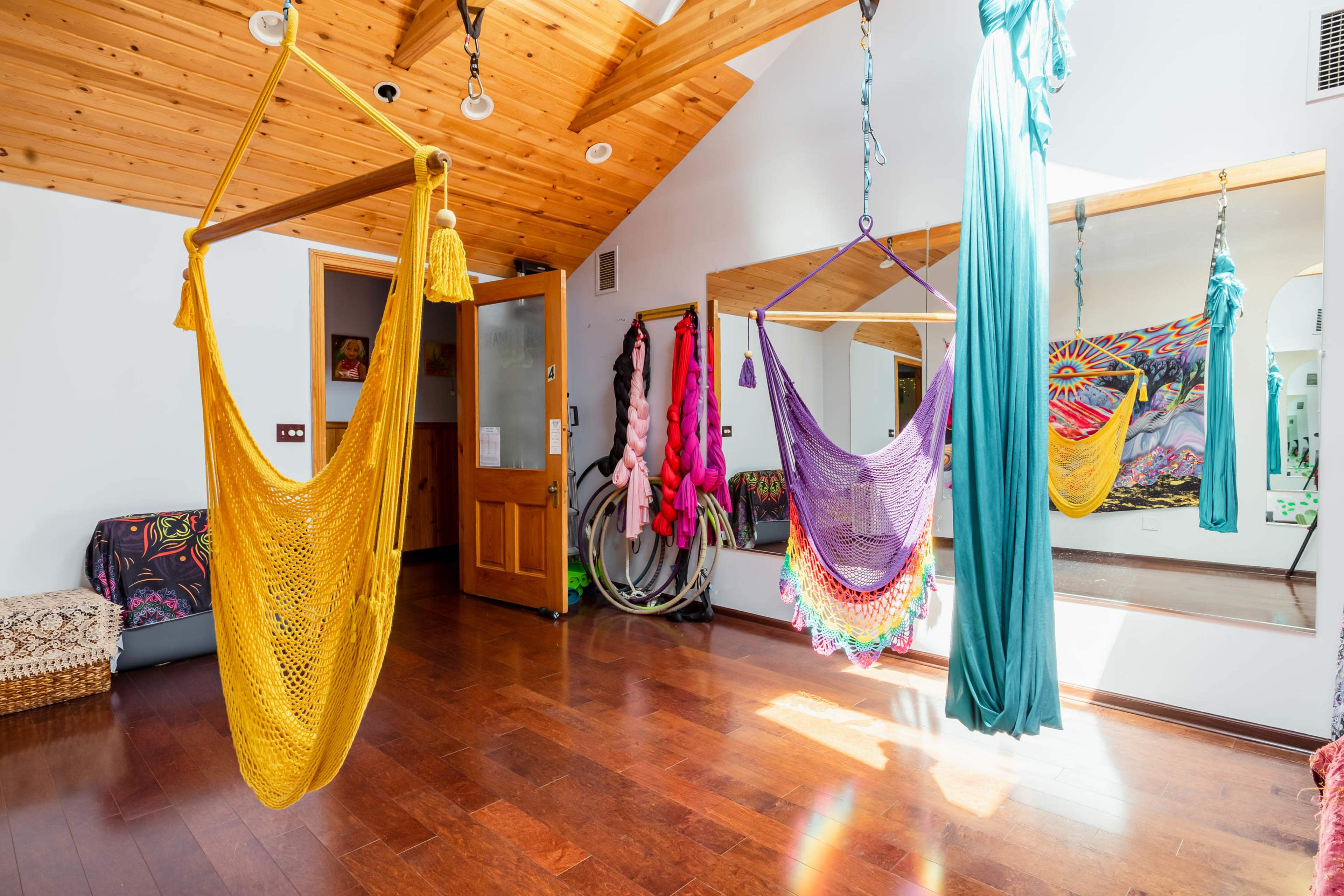 The room features colorful hanging hammocks, wooden ceilings, and a mirror reflecting vibrant wall decorations.