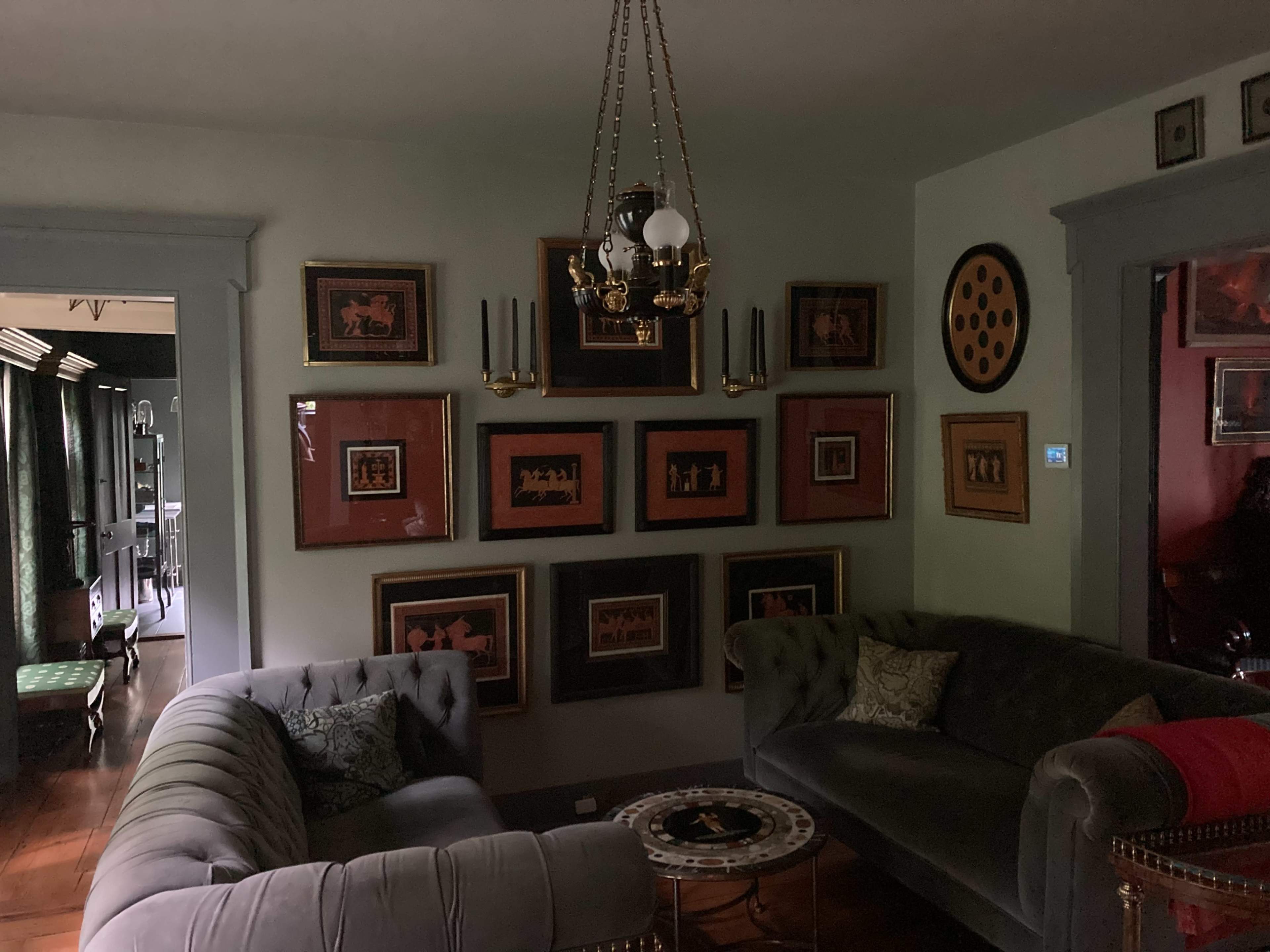 A dimly lit living room with two sofas, a central coffee table, and a wall adorned with framed artwork and decorative items.