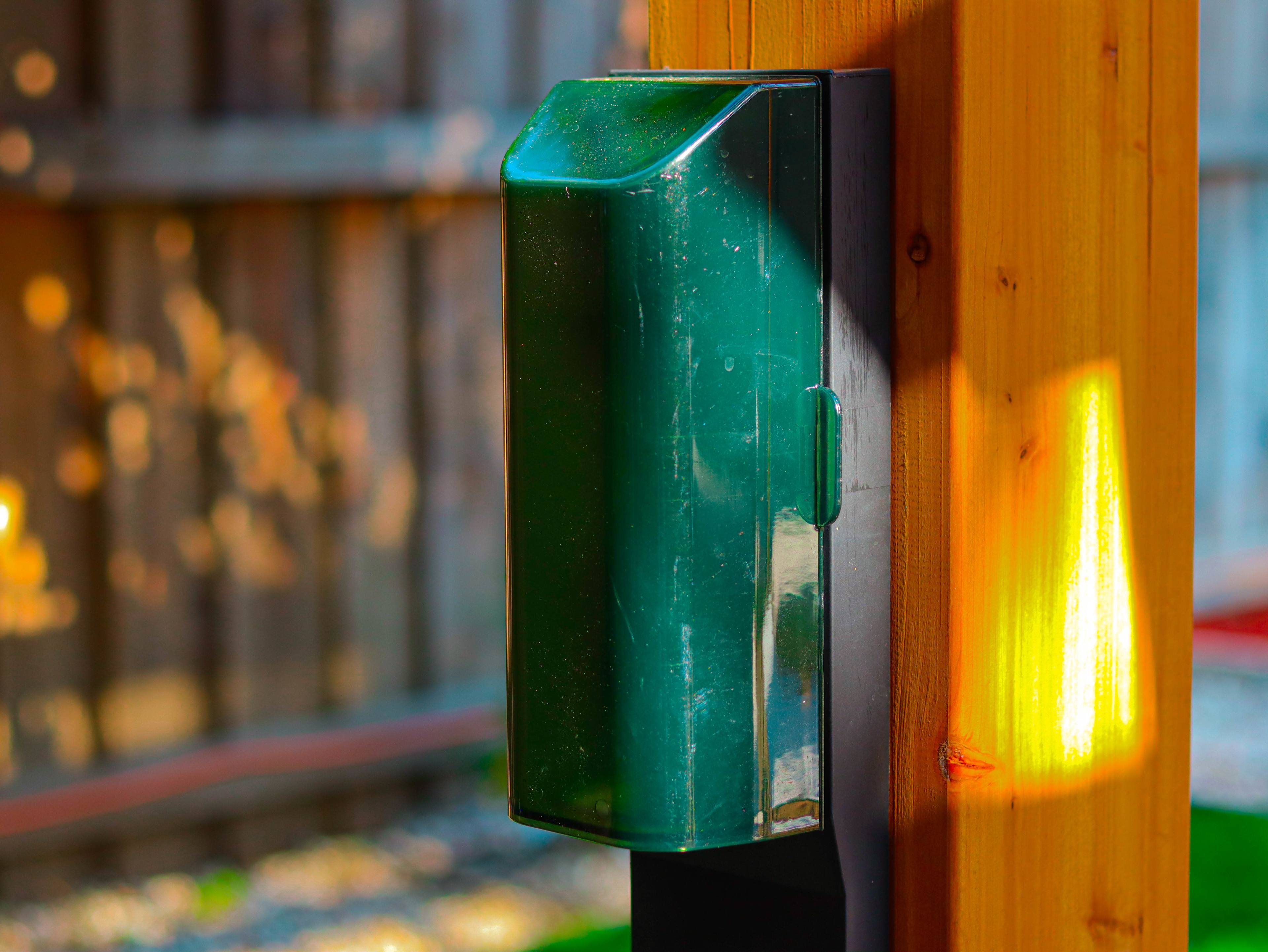 A green mailbox is mounted on a wooden post with sunlight highlighting its surface.