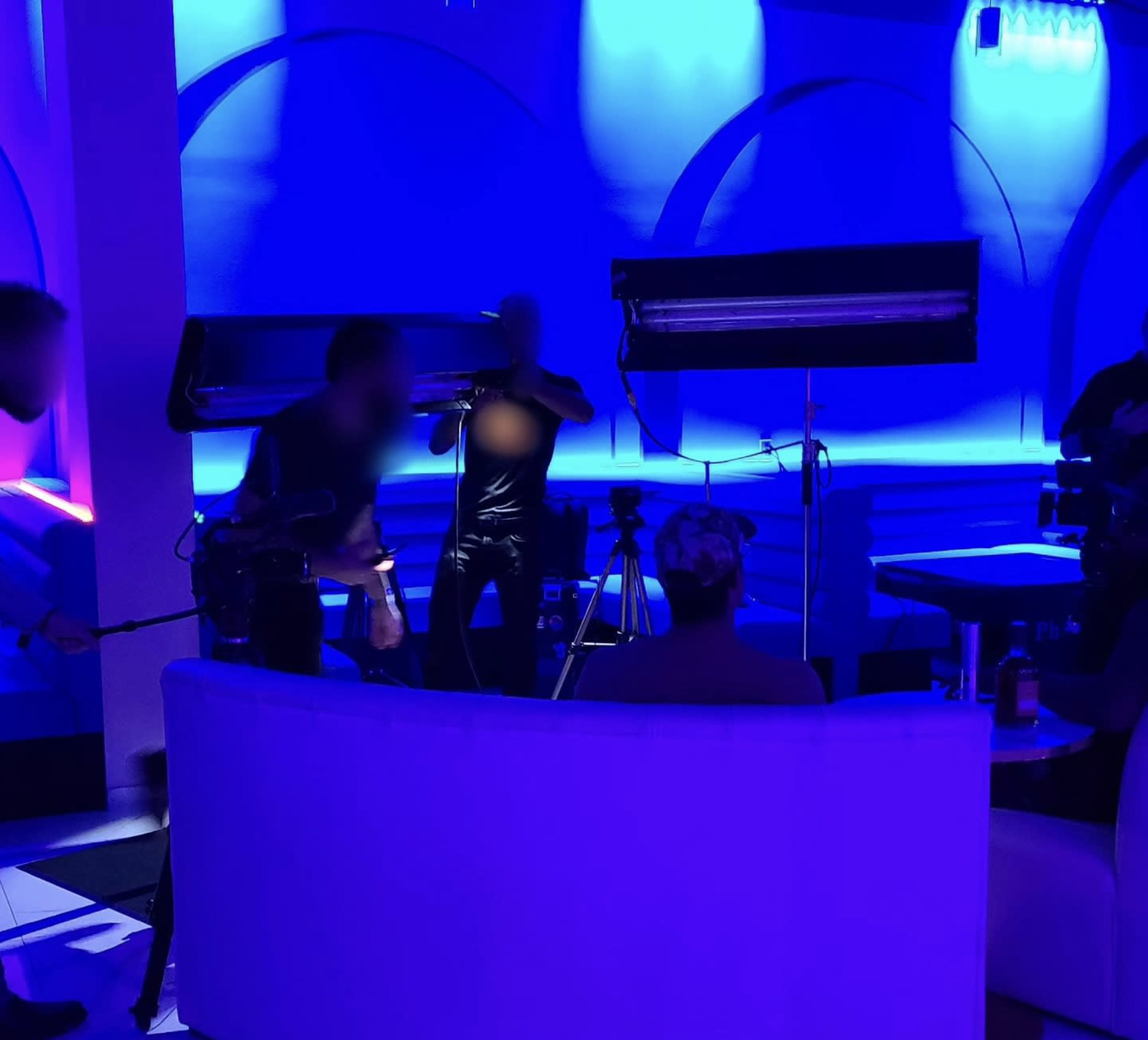 A film crew sets up equipment in a dimly lit, blue-toned room for a recording session.