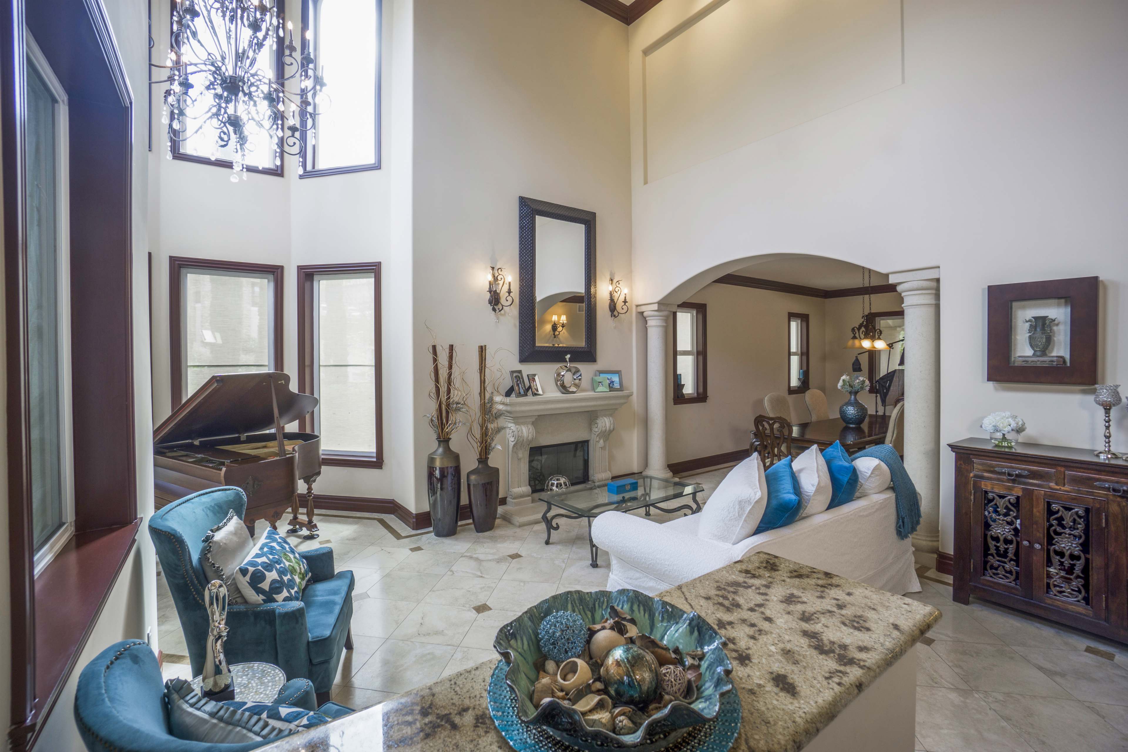 The image showcases a spacious living room featuring a grand piano, elegant furniture, and large windows that allow natural light to fill the space.