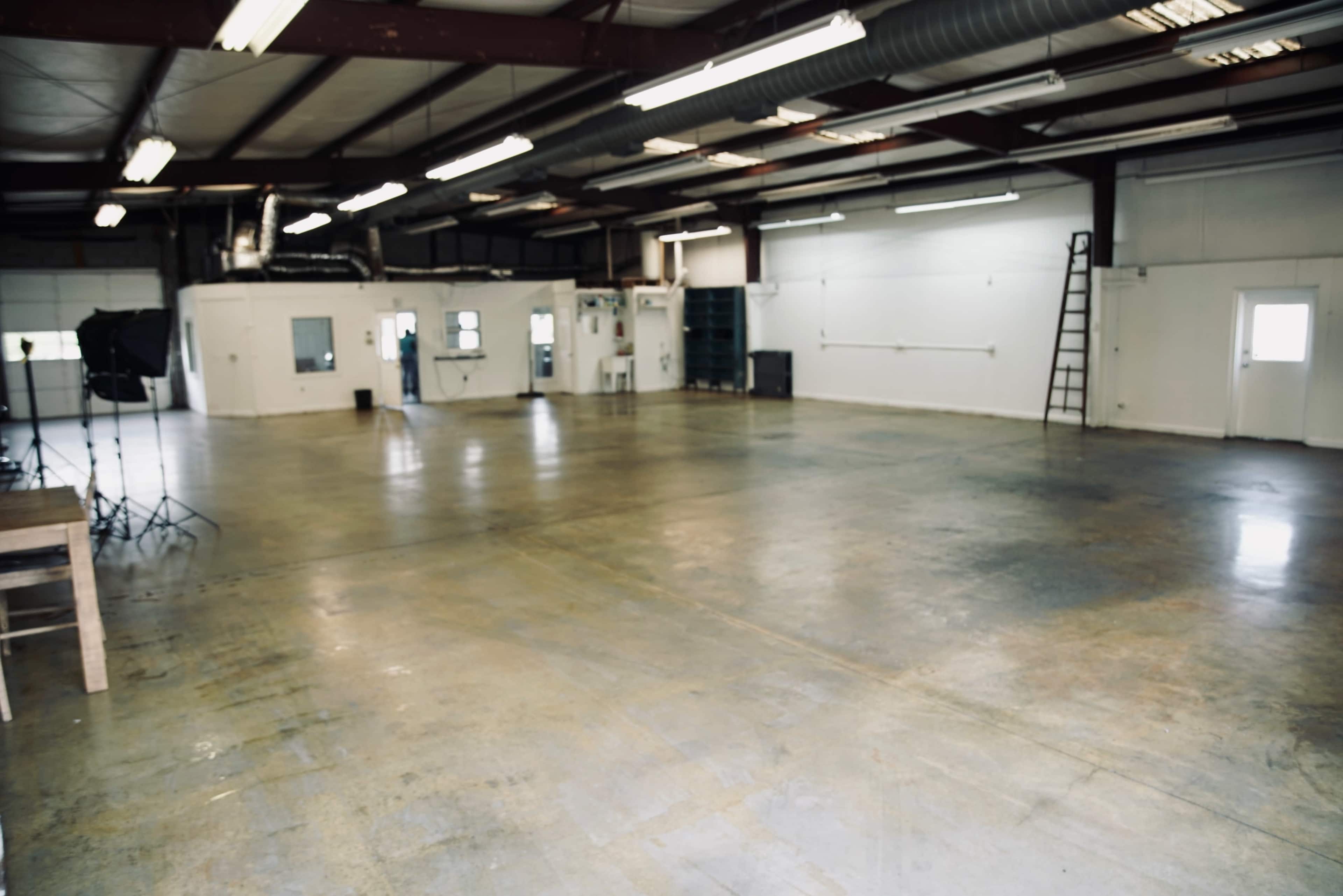 The image shows a large, empty industrial space with concrete floors and overhead lighting.