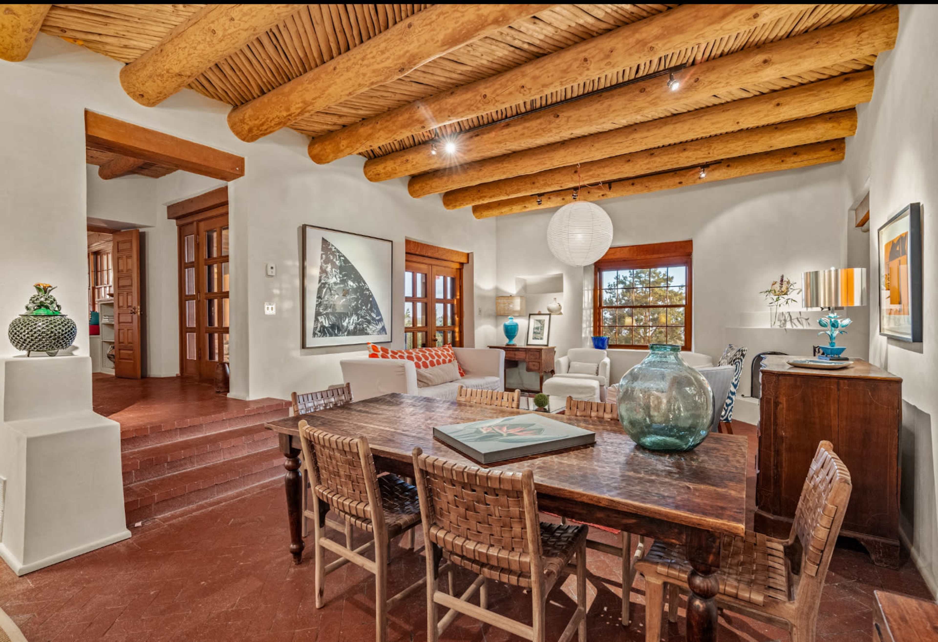 A spacious living area features wooden beams, a large dining table, and various decorative elements.