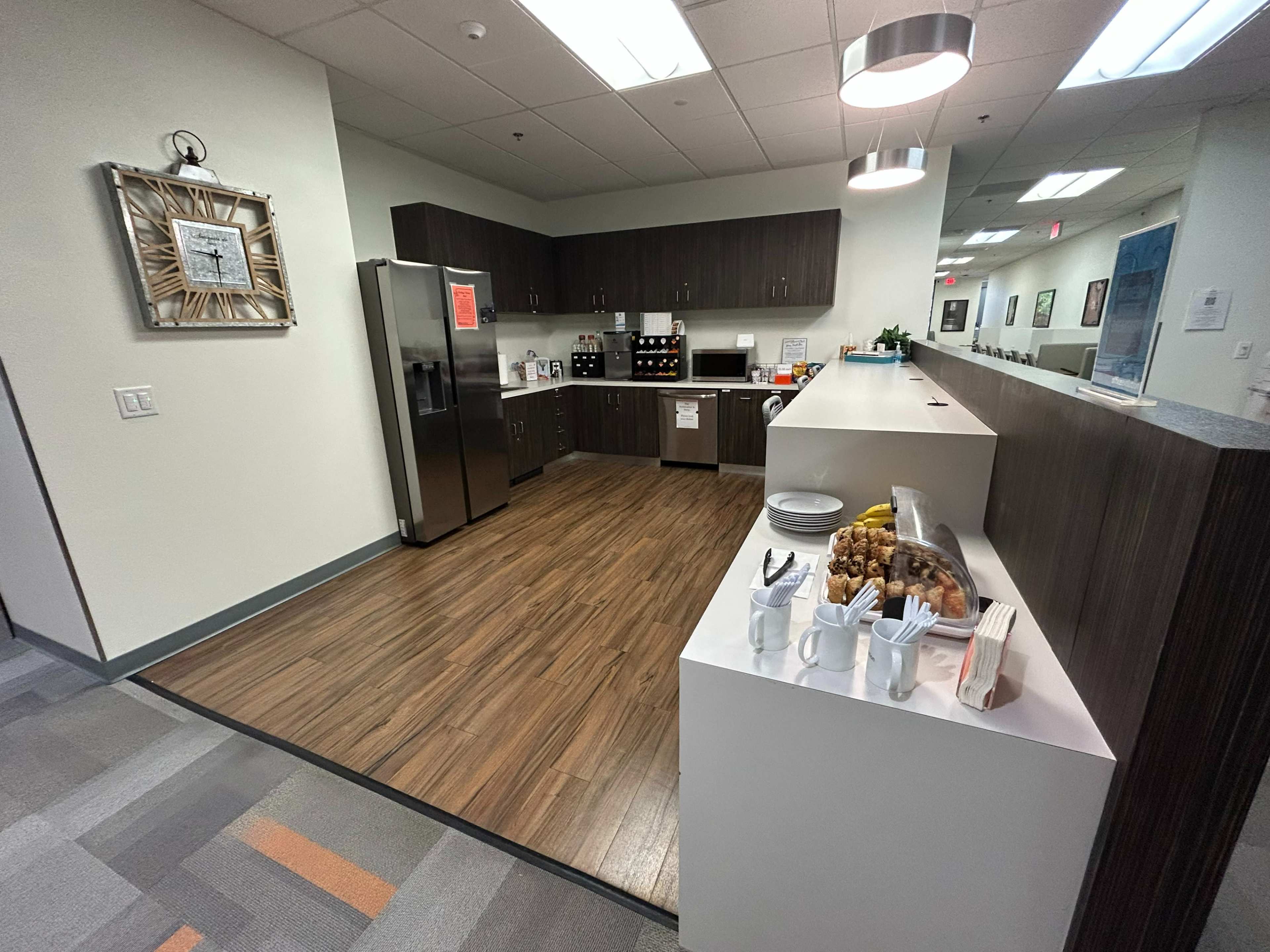 The image shows a modern kitchen area with a large refrigerator, cabinets, and a counter displaying snacks and drinks.