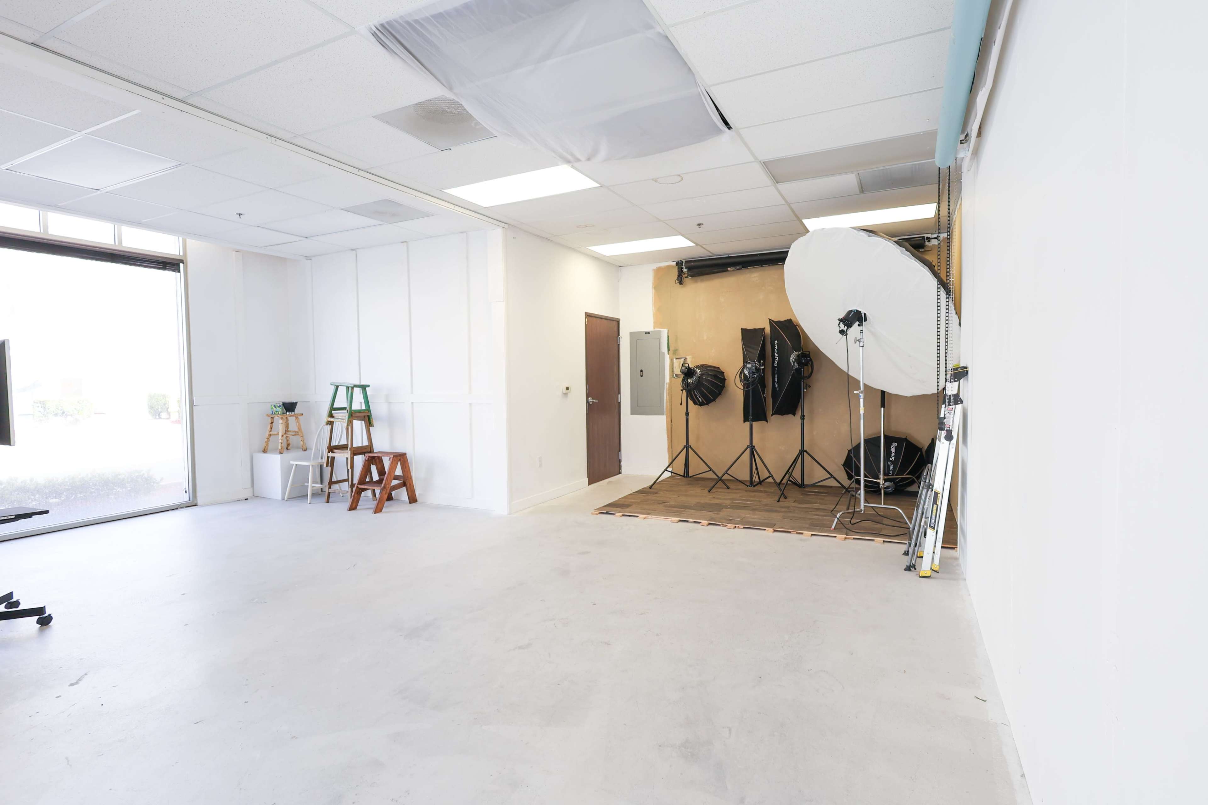 The image shows a spacious photography studio with a large backdrop setup, lighting equipment, and minimal furniture.