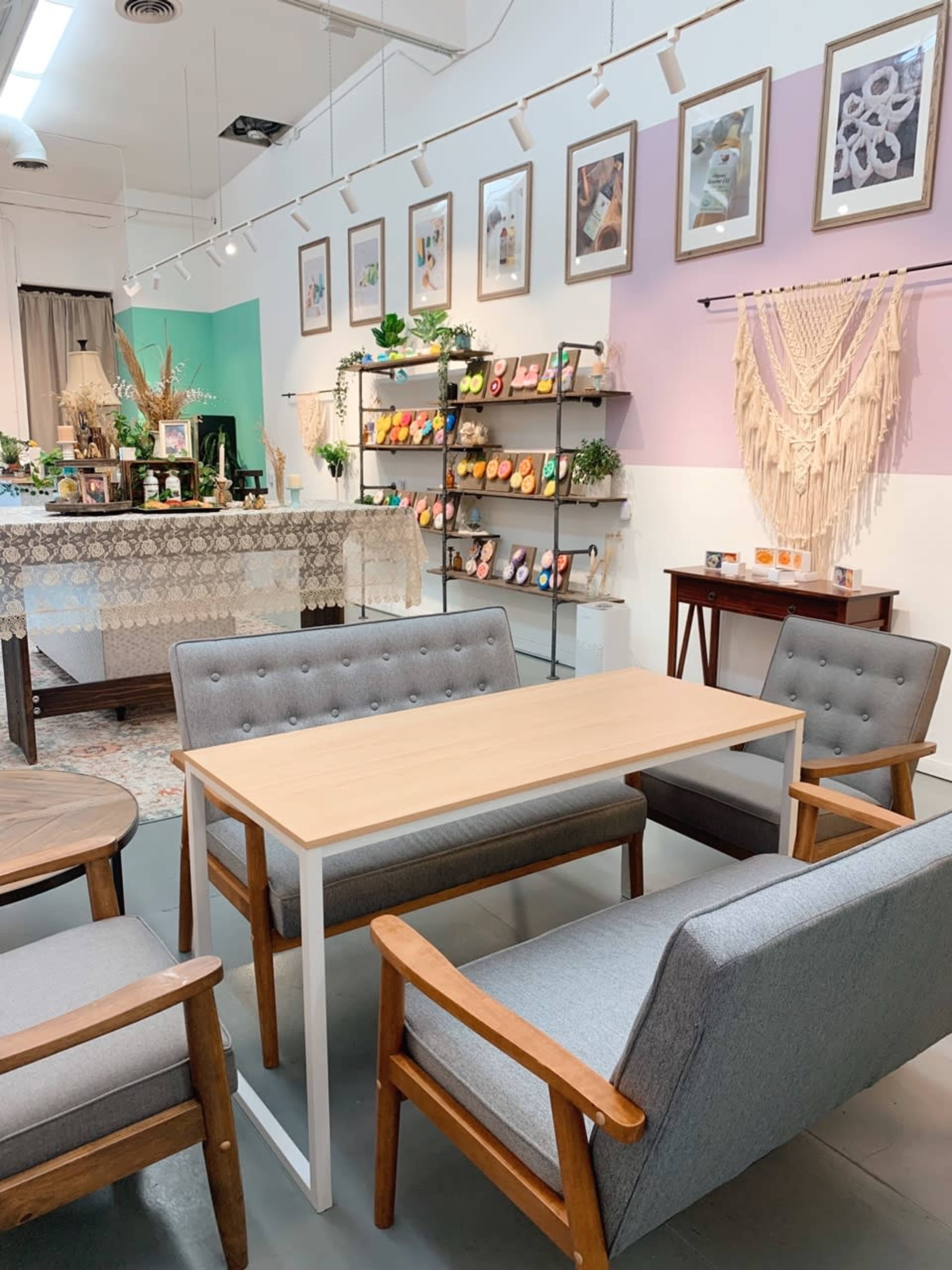 A cozy interior space with a light wooden table and gray seating arranged, surrounded by decorative wall art and various plants on shelves.