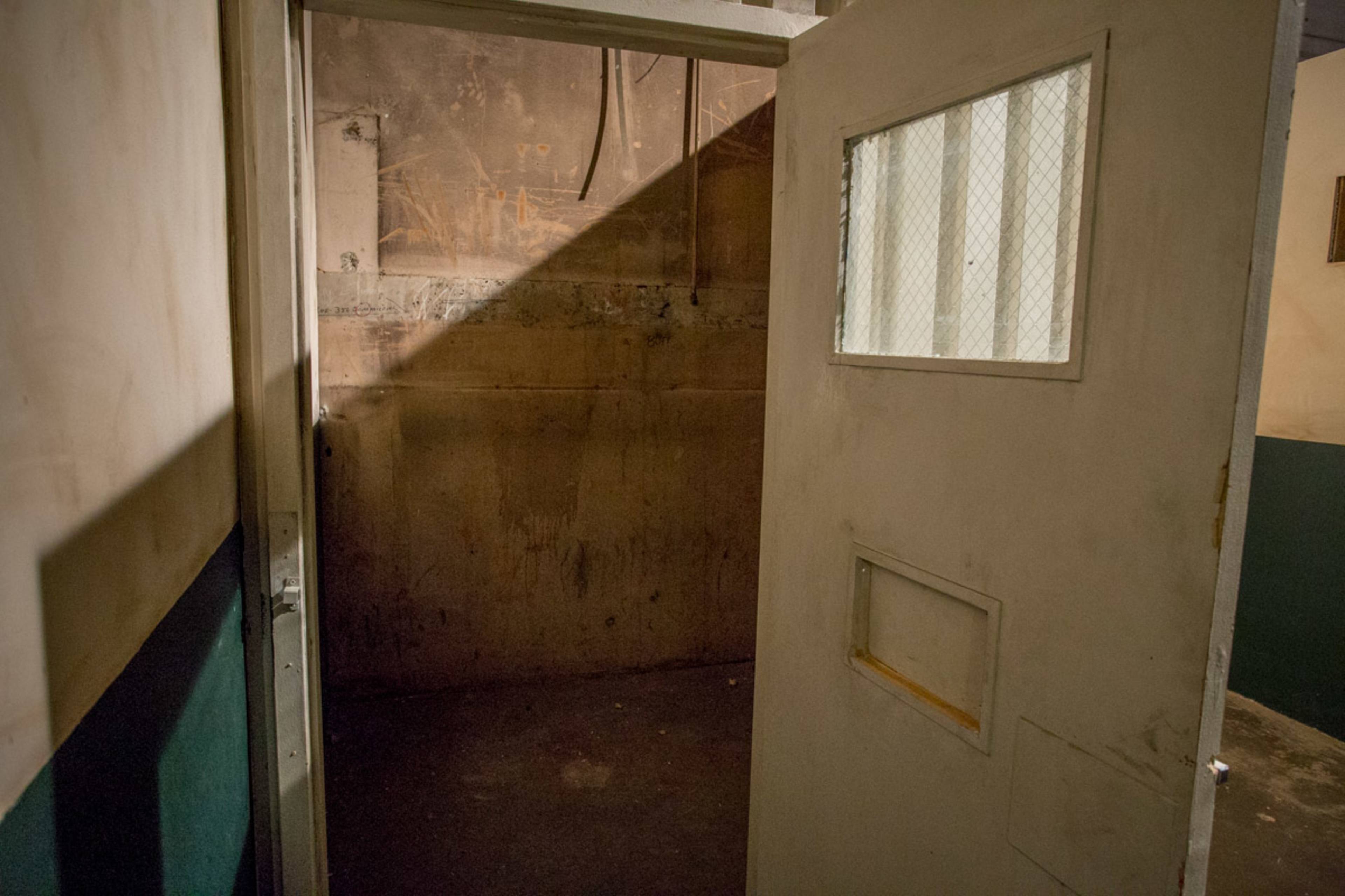 A partially opened door reveals a dimly lit, empty room with a concrete floor and bare walls.