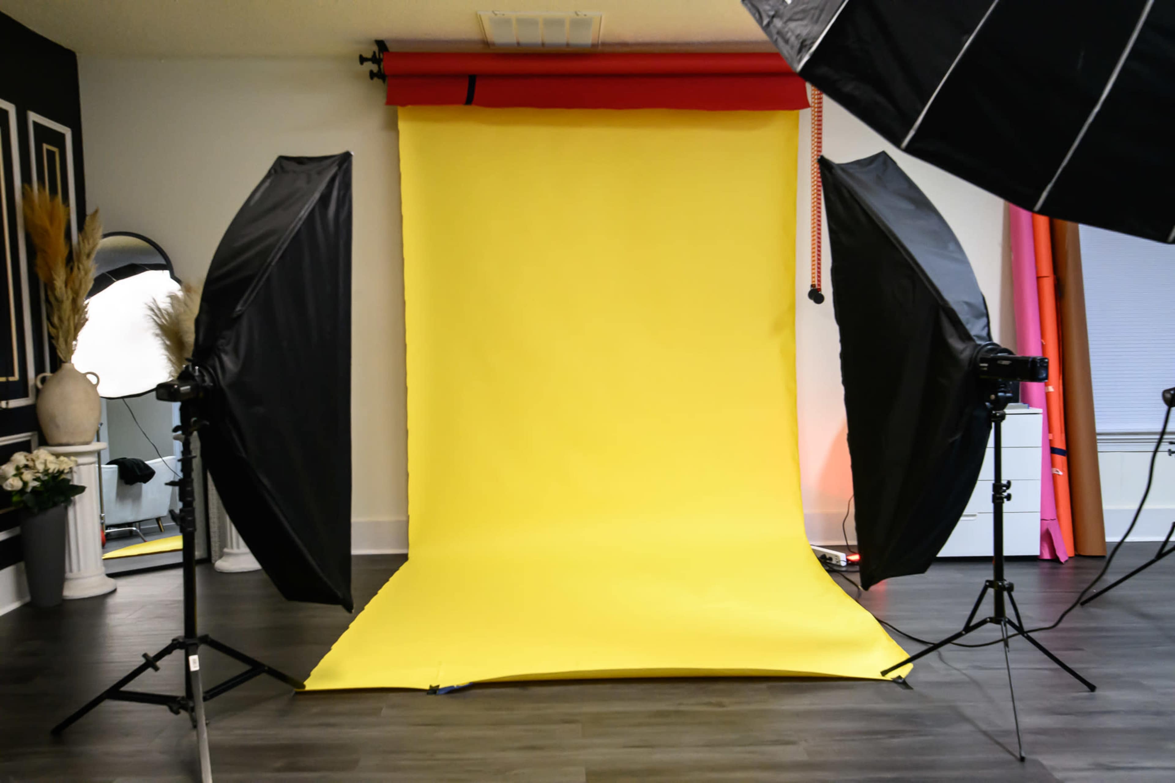 A photography studio features a vibrant yellow backdrop, flanked by large softbox lights on either side.