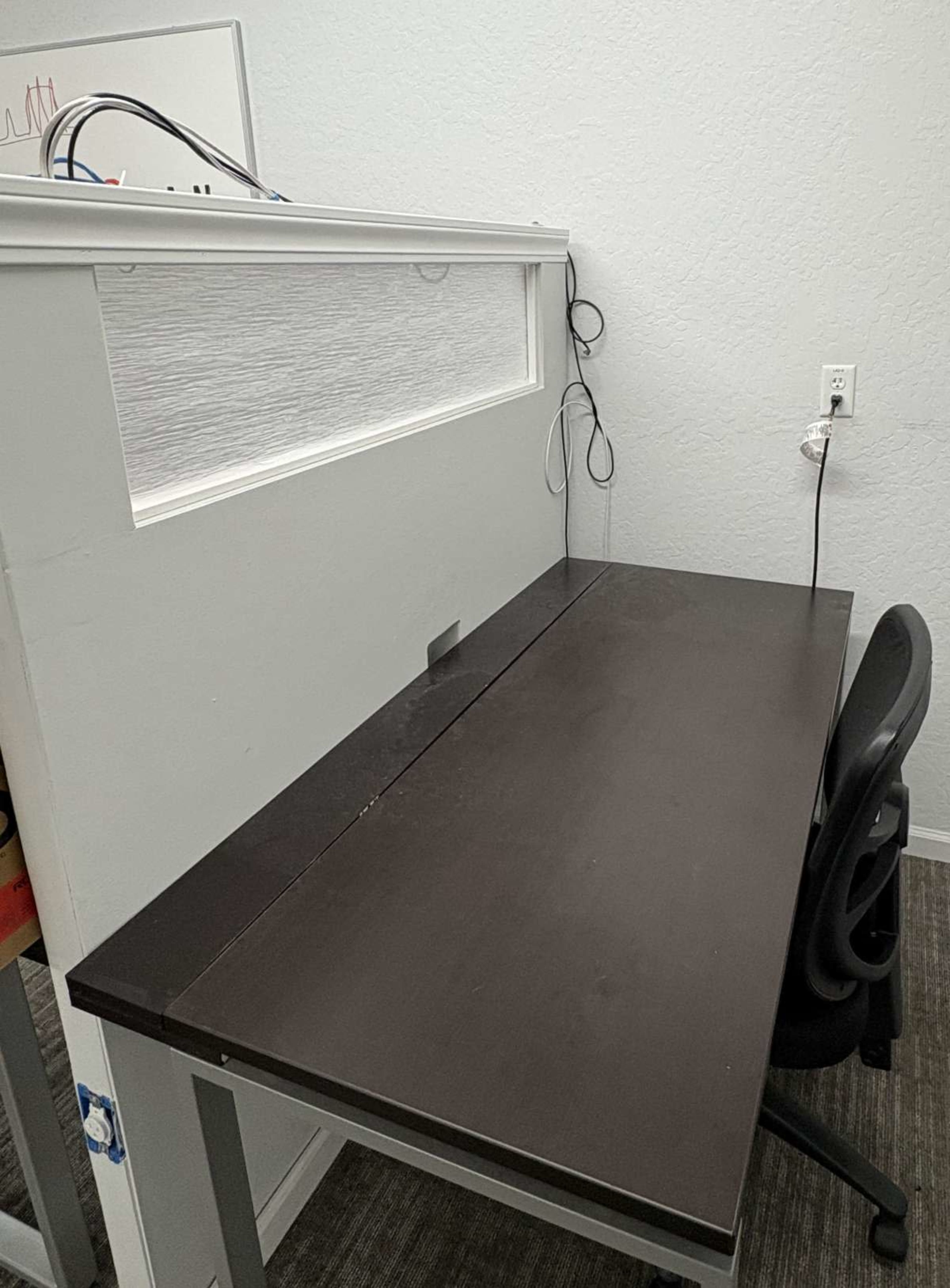 A simple office space features a dark wood desk, a black chair, and a wall with a horizontal window.