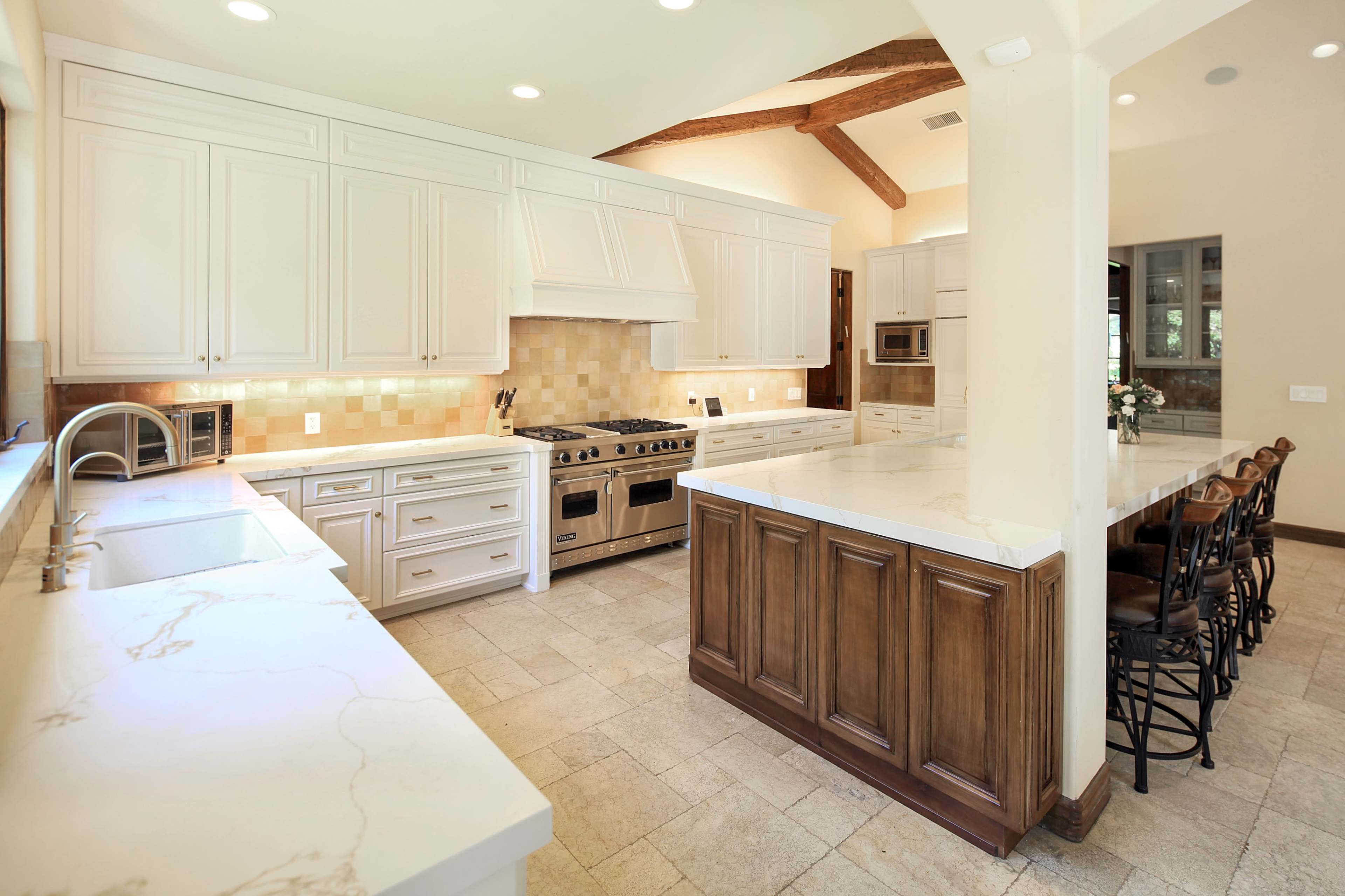 A spacious kitchen with white cabinets, a large island with wooden cabinetry, and stainless steel appliances.