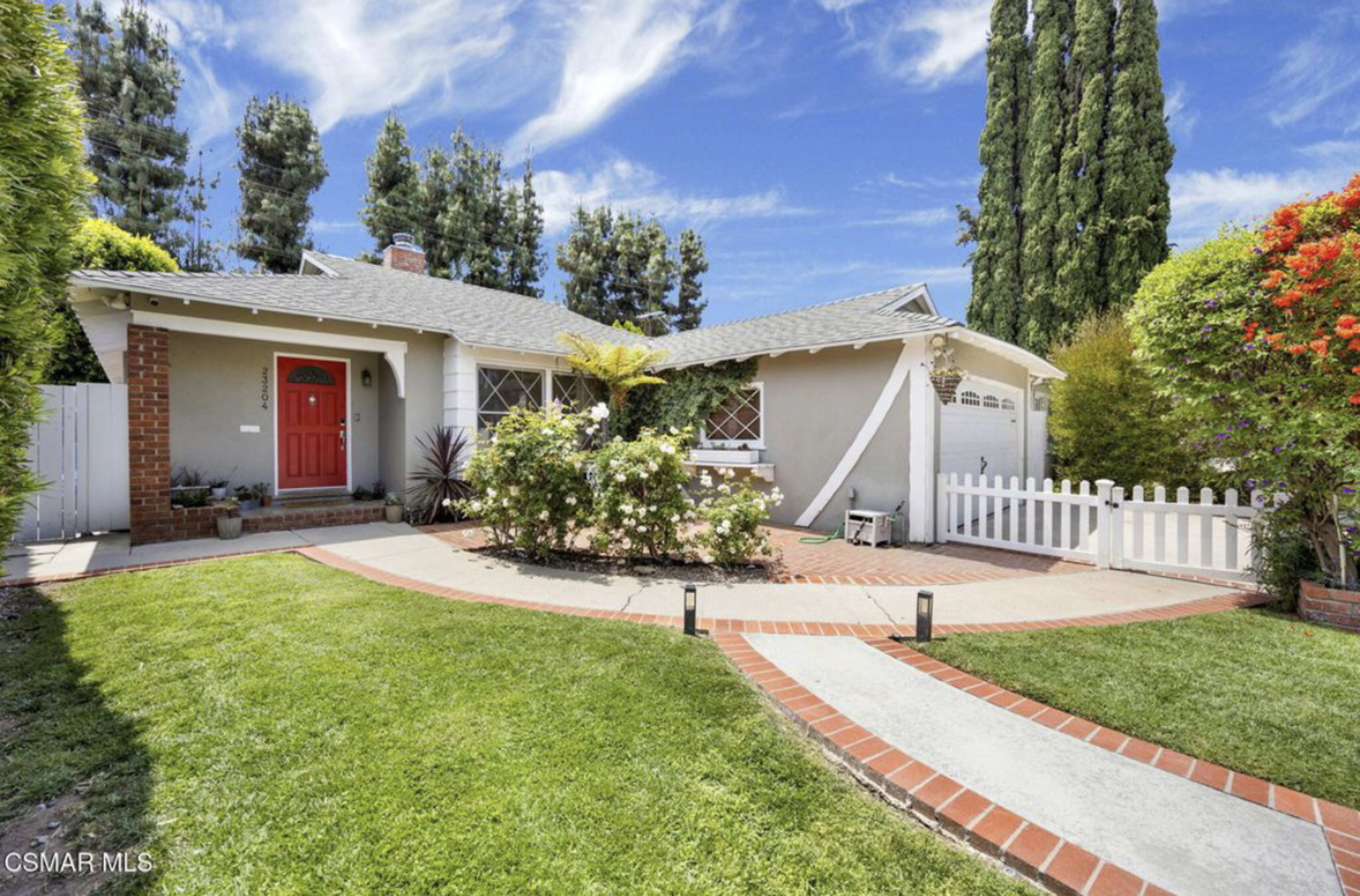 A single-story house with a red front door and a neatly landscaped yard featuring a path and white picket fence.