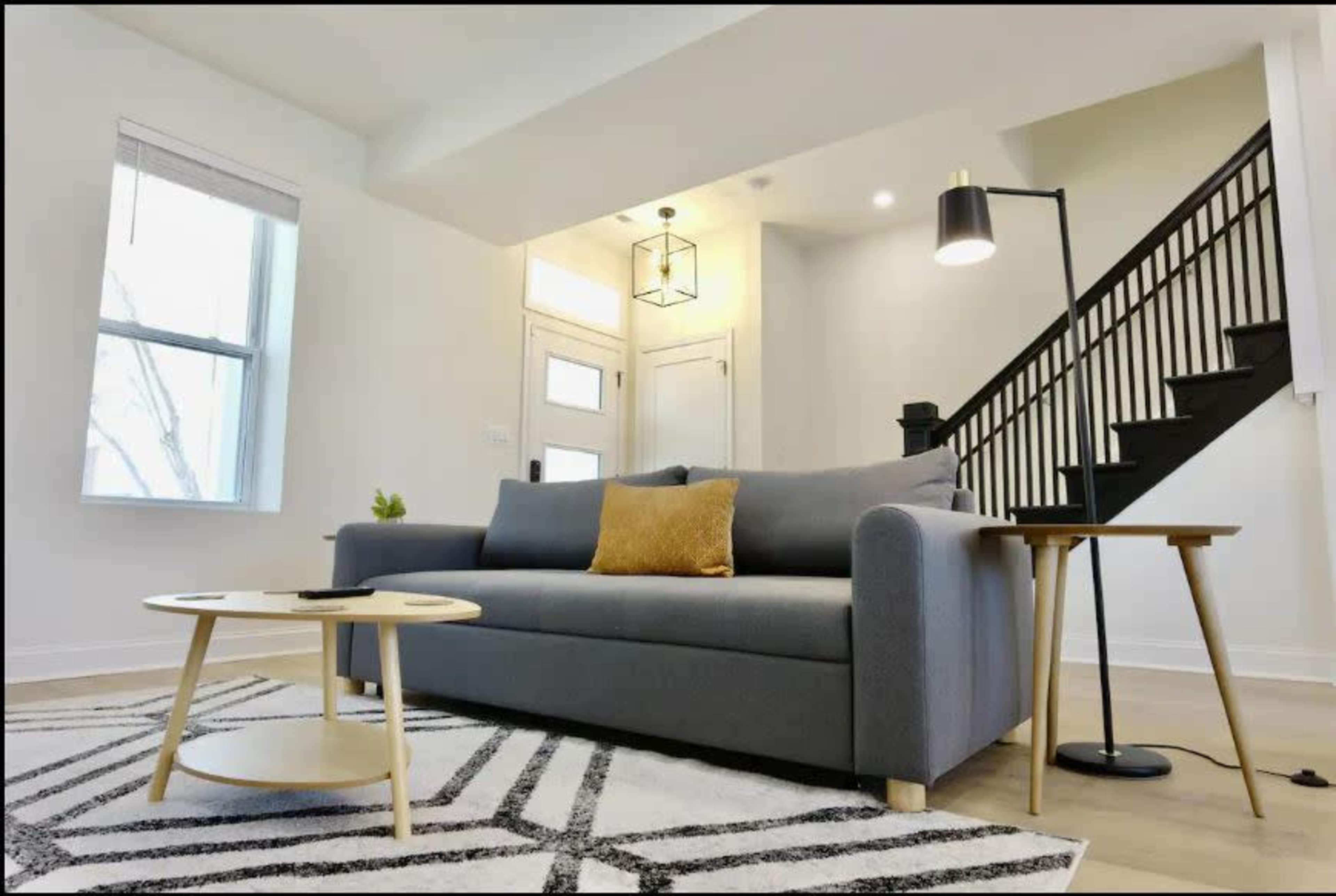 A modern living room with a gray sofa, a round wooden coffee table, a floor lamp, and a staircase in the background.