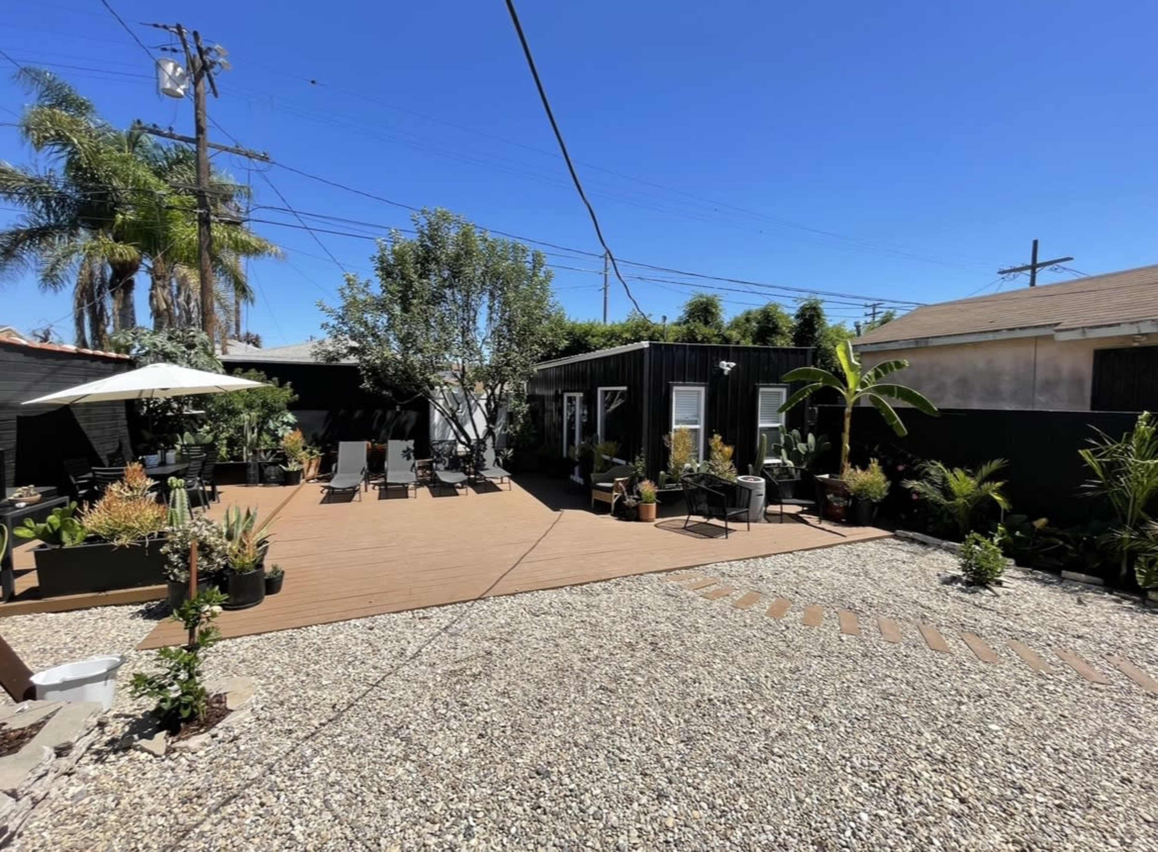 A landscaped backyard featuring a deck area with lounge chairs, several potted plants, and a small building surrounded by gravel.