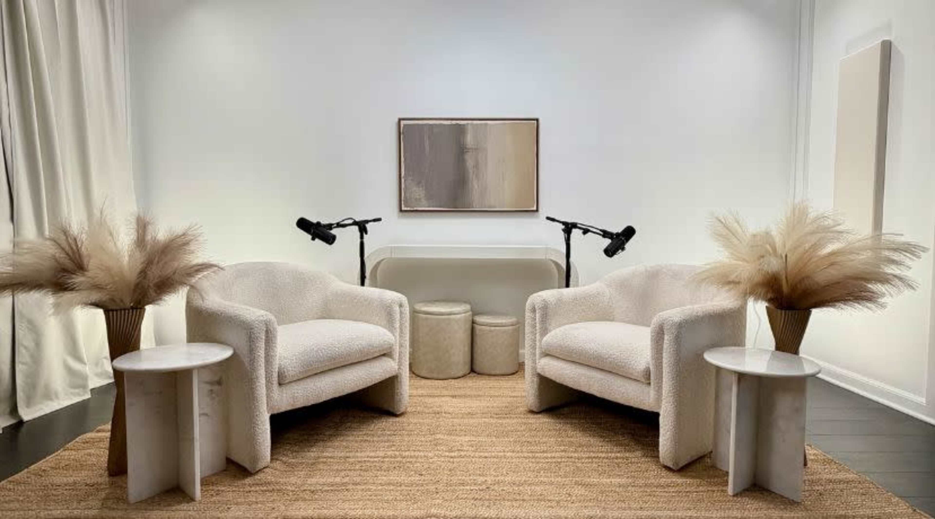 The image features two plush armchairs facing each other, accompanied by small round tables and decorative vases with dried plants, all set against a minimalist backdrop.