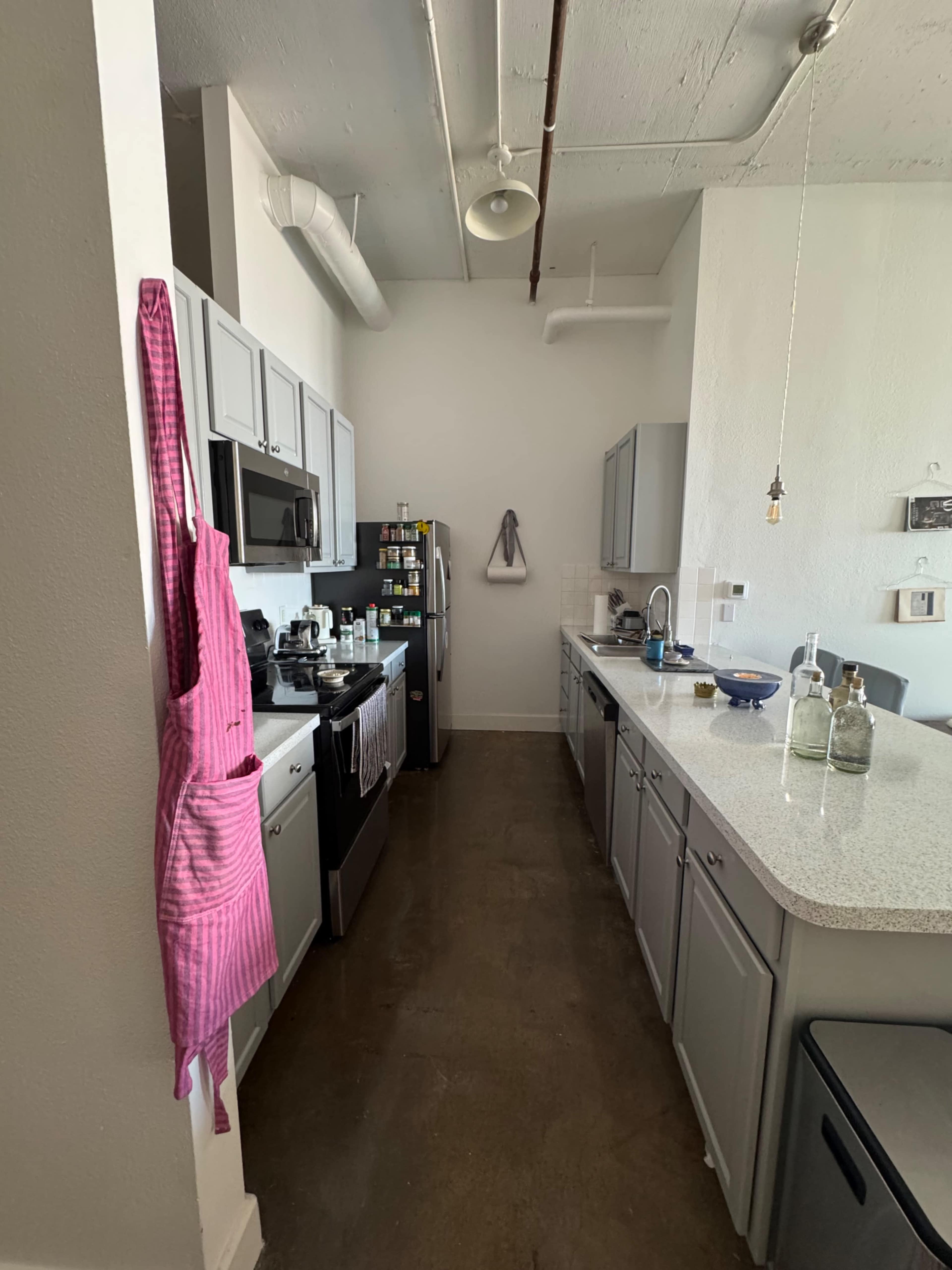 The image shows a modern kitchen with gray cabinets, stainless steel appliances, and a countertop that includes various cooking items and utensils.