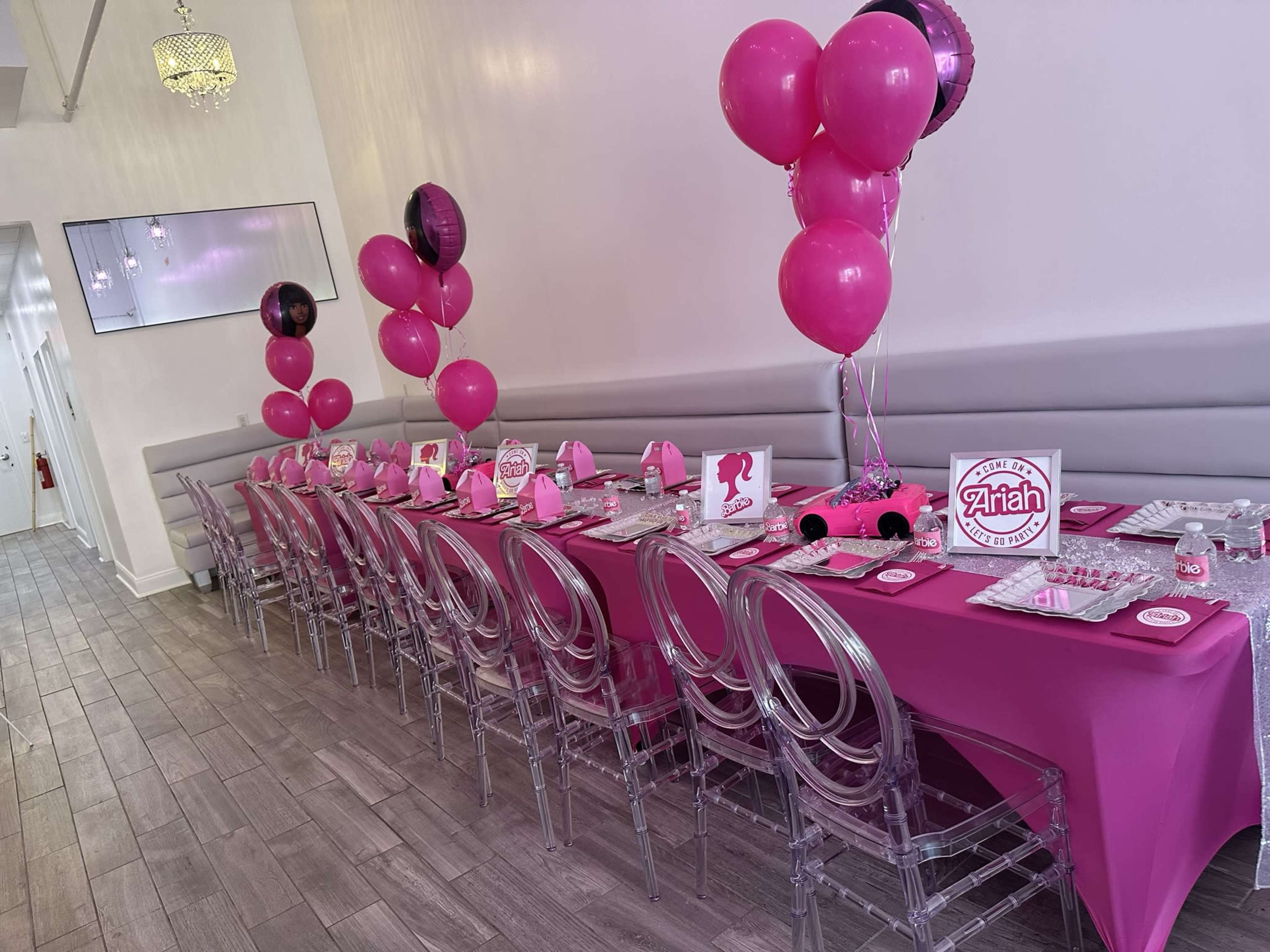 A long, elegantly set party table is adorned with pink decorations, balloons, and themed party supplies.