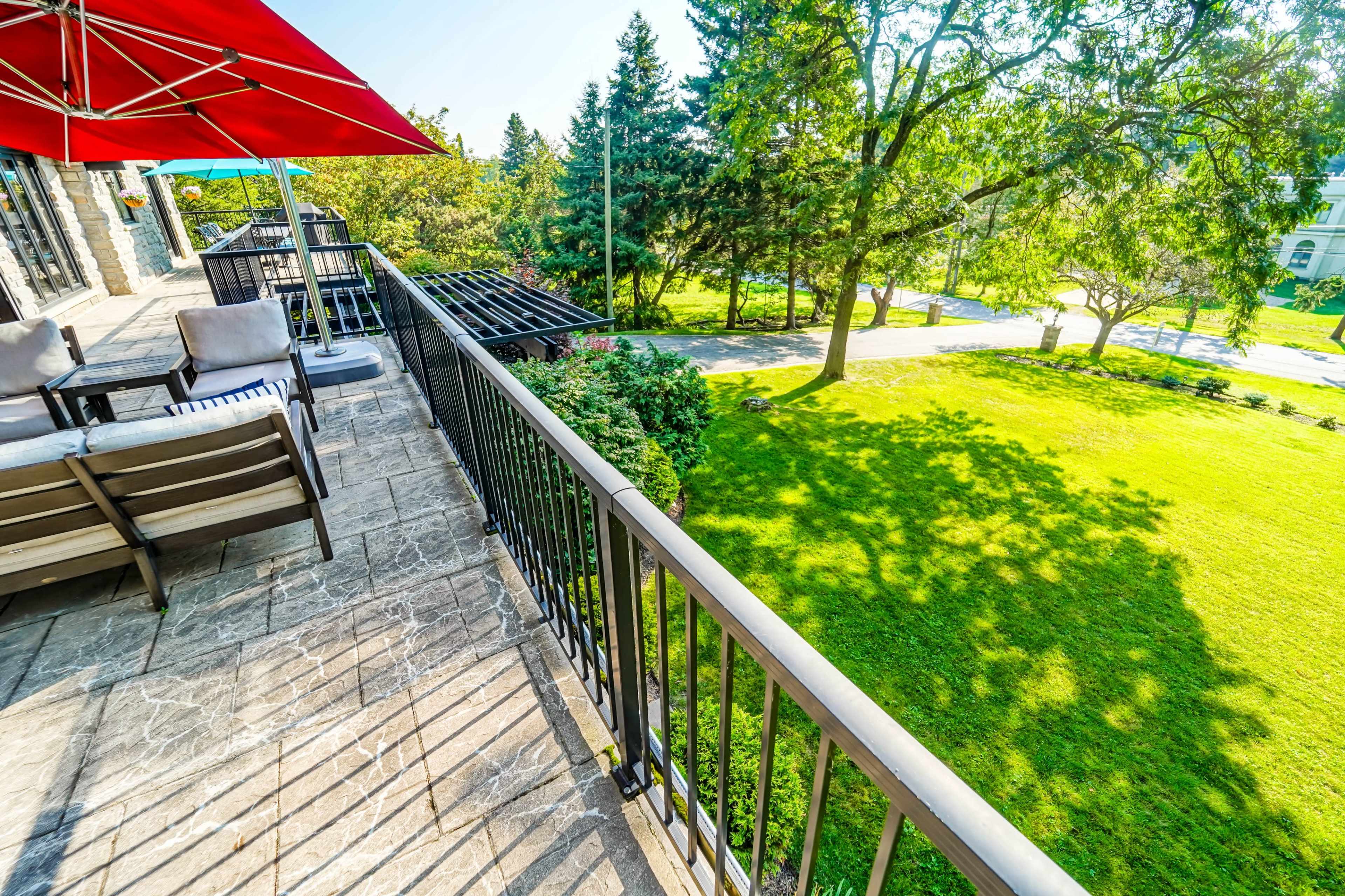A balcony with seating overlooks a green lawn and trees under a clear blue sky.