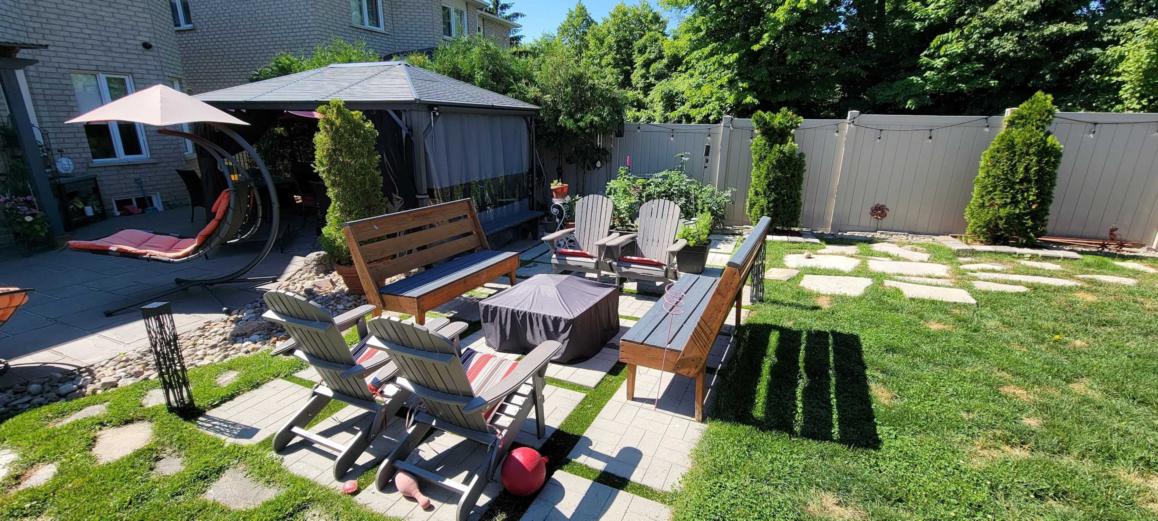 A backyard patio area with seating arrangements, a gazebo, and a landscaped garden featuring stone pathways and grassy patches.