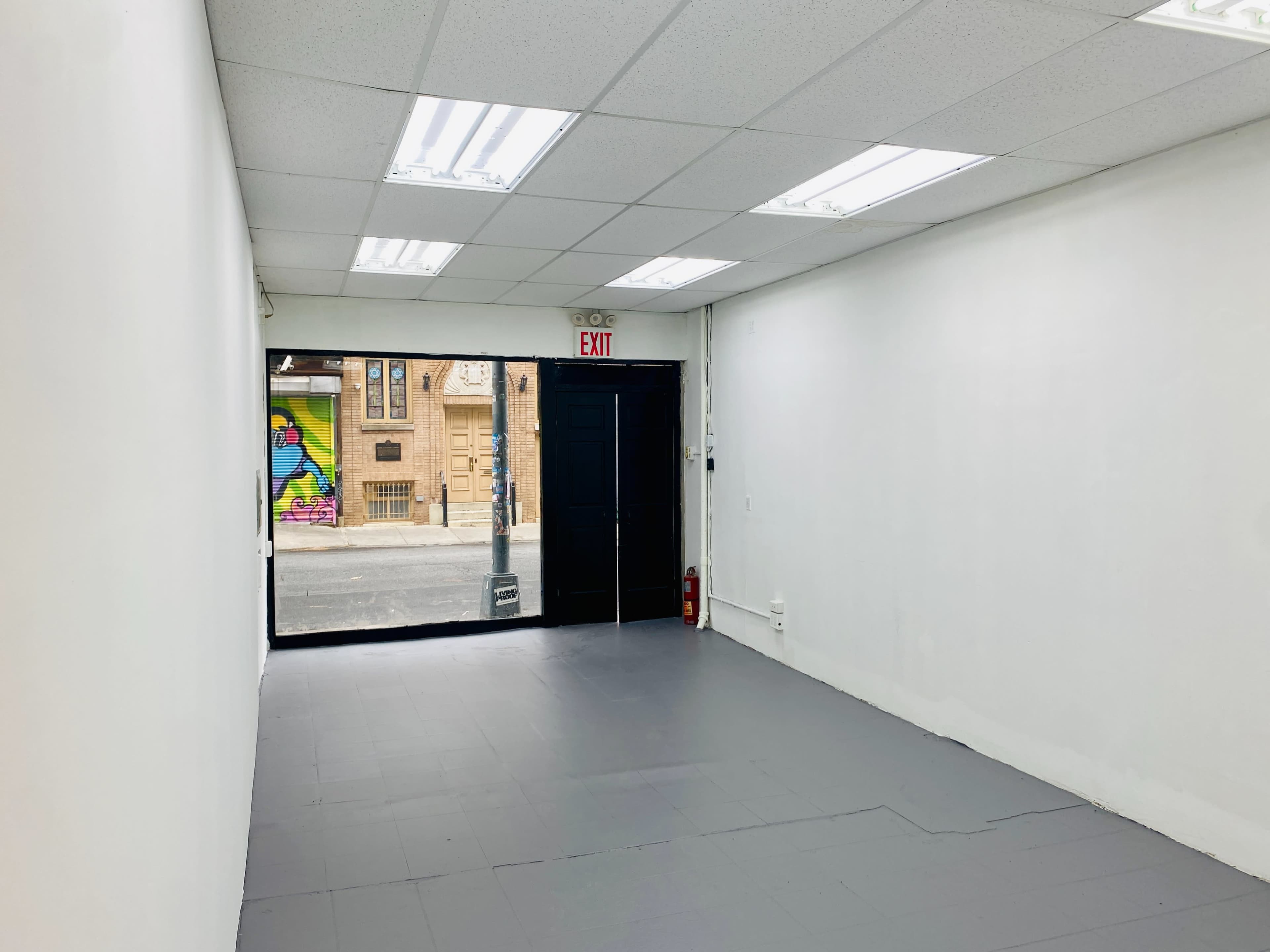 An empty interior room with gray flooring and a door leading to a street featuring colorful graffiti.