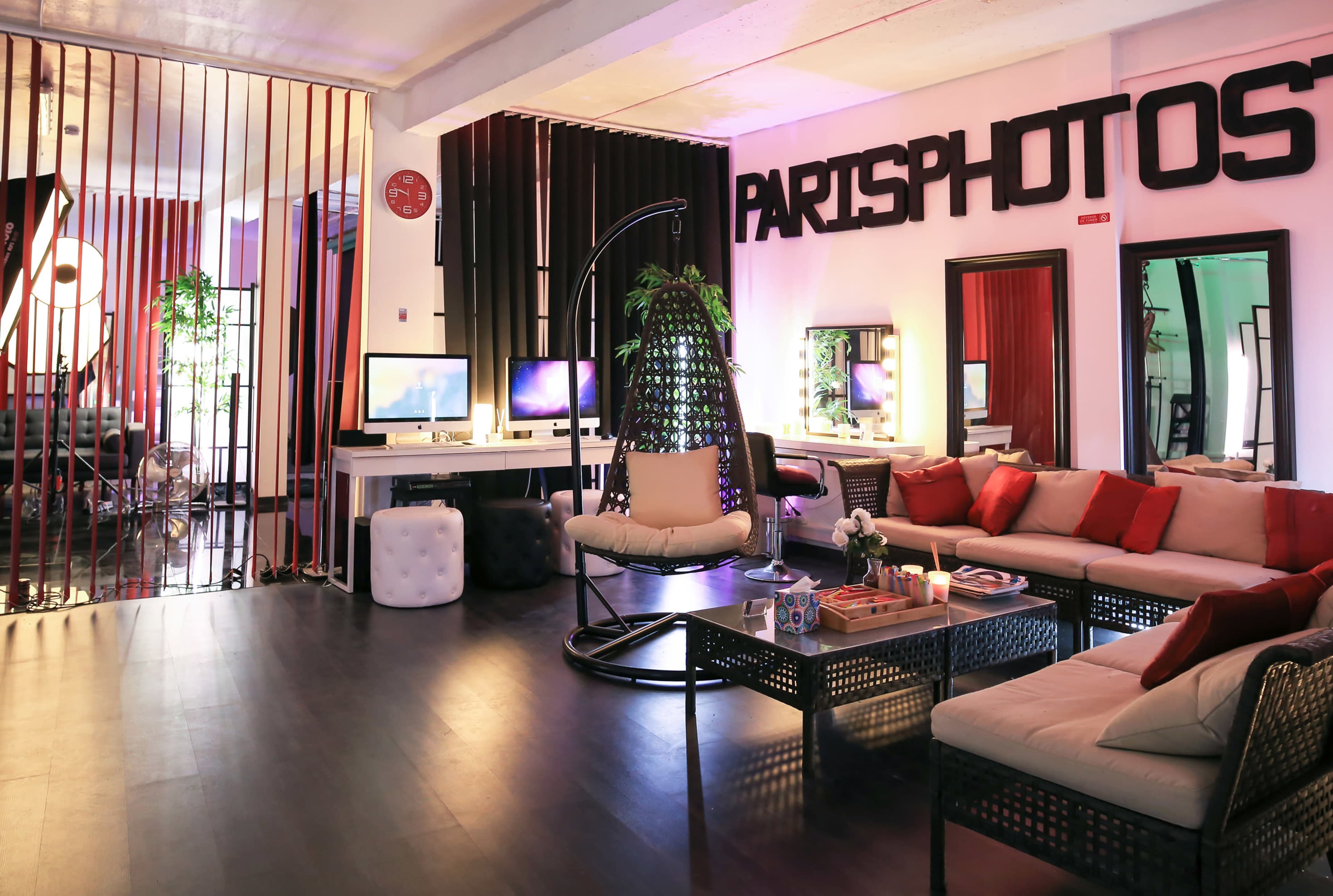The image depicts a modern studio space with a lounge area featuring comfortable seating, decorative plants, and large screens against a backdrop of bold wall signage.