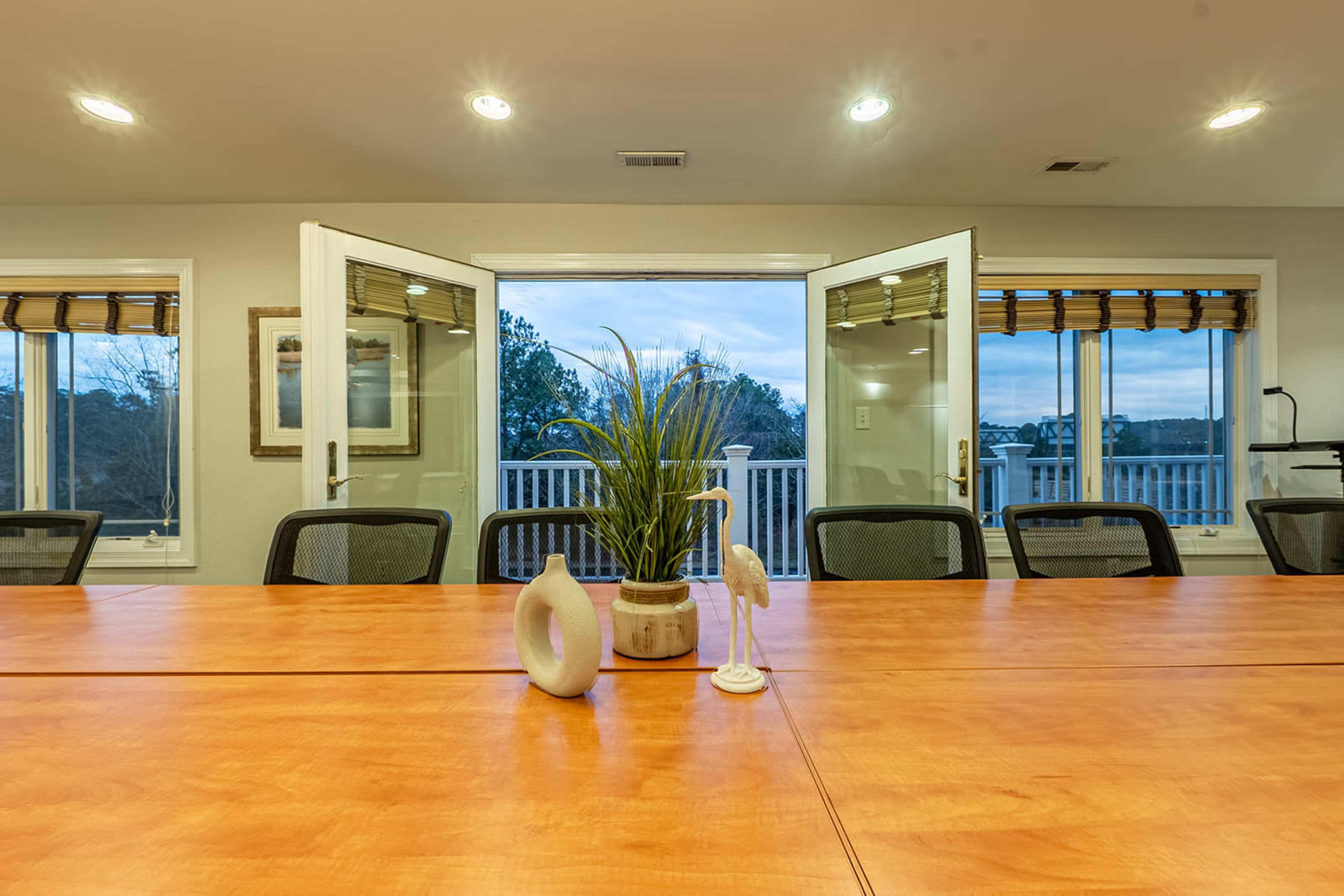 A conference room features a wooden table with a plant centerpiece, flanked by two sets of French doors that open to a view outside.