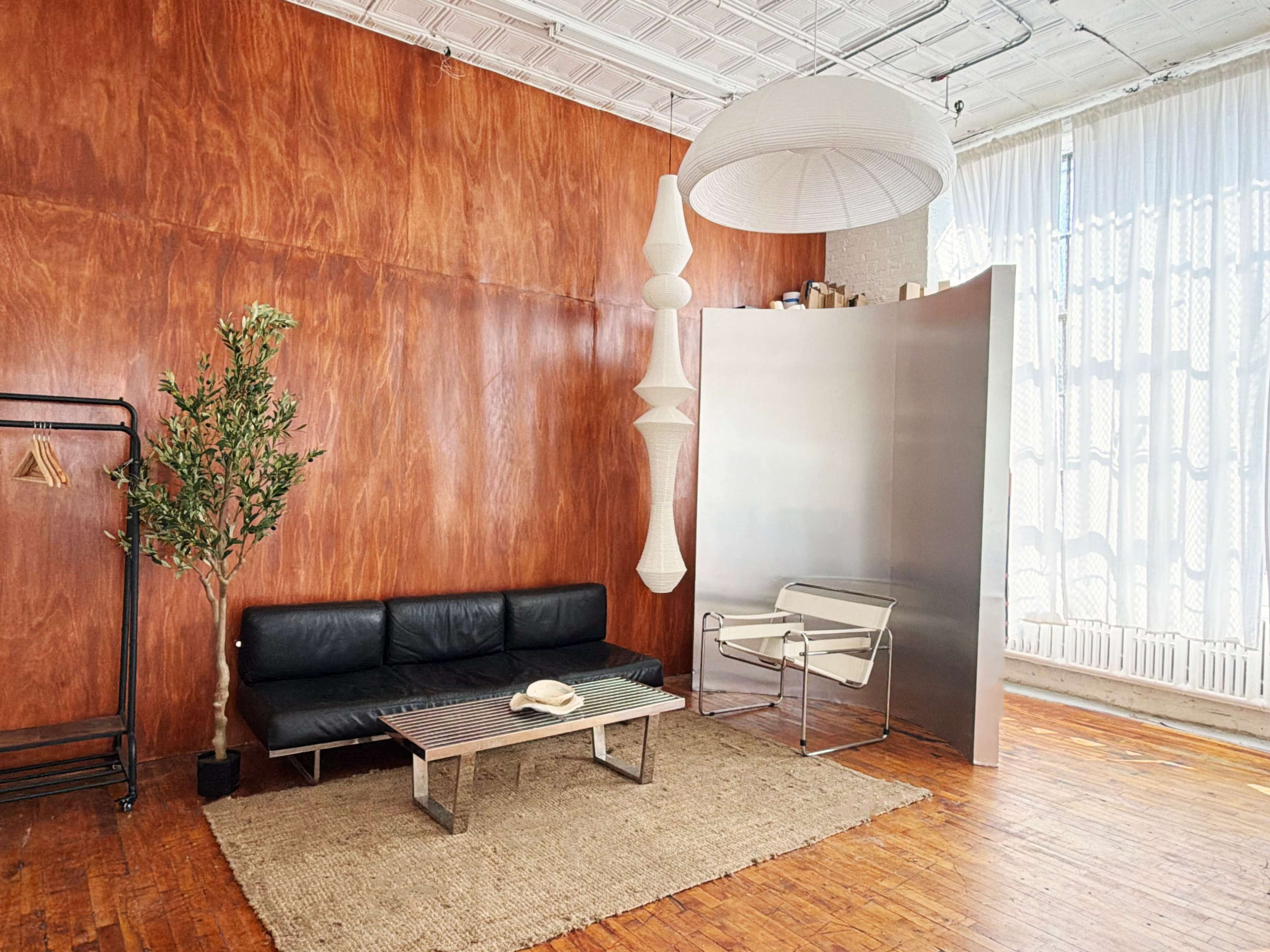 The image features a modern interior with wood-paneled walls, a black sofa, a minimalist table, a light-hanging fixture, and a decorative plant.