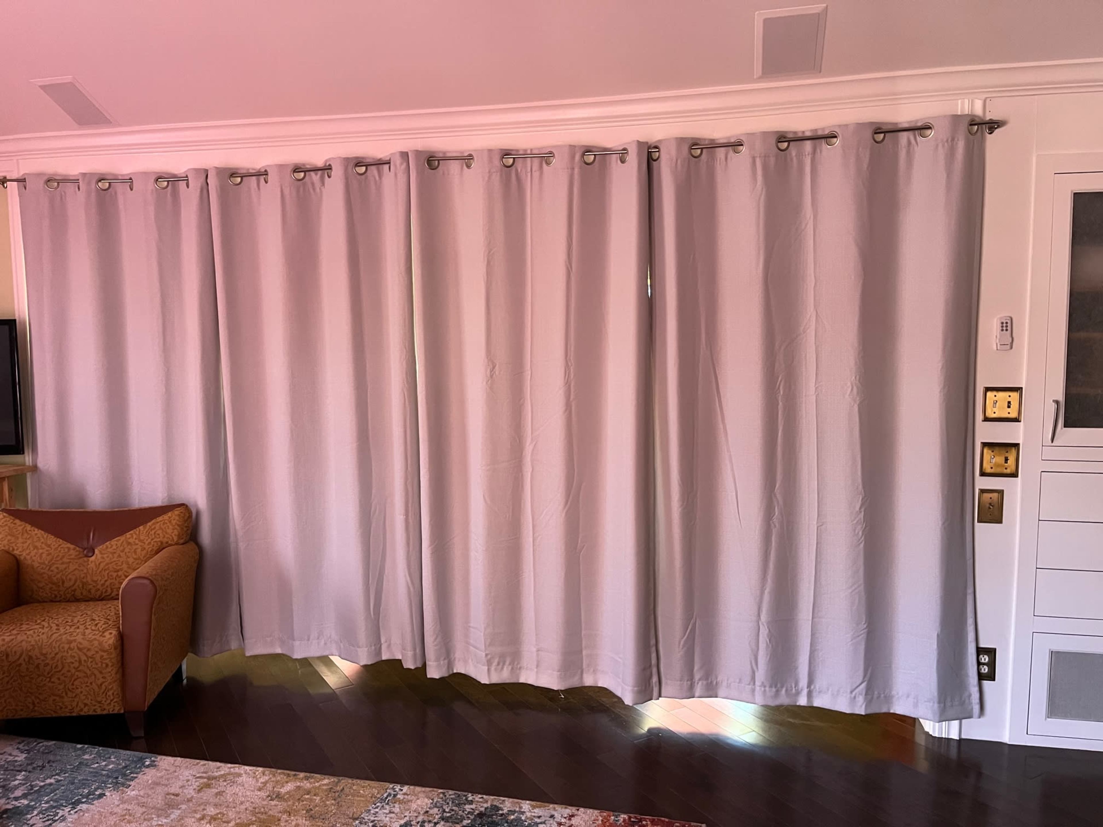 A set of light-colored curtains hangs over a window in a room with hardwood flooring, accompanied by a patterned sofa to the left.