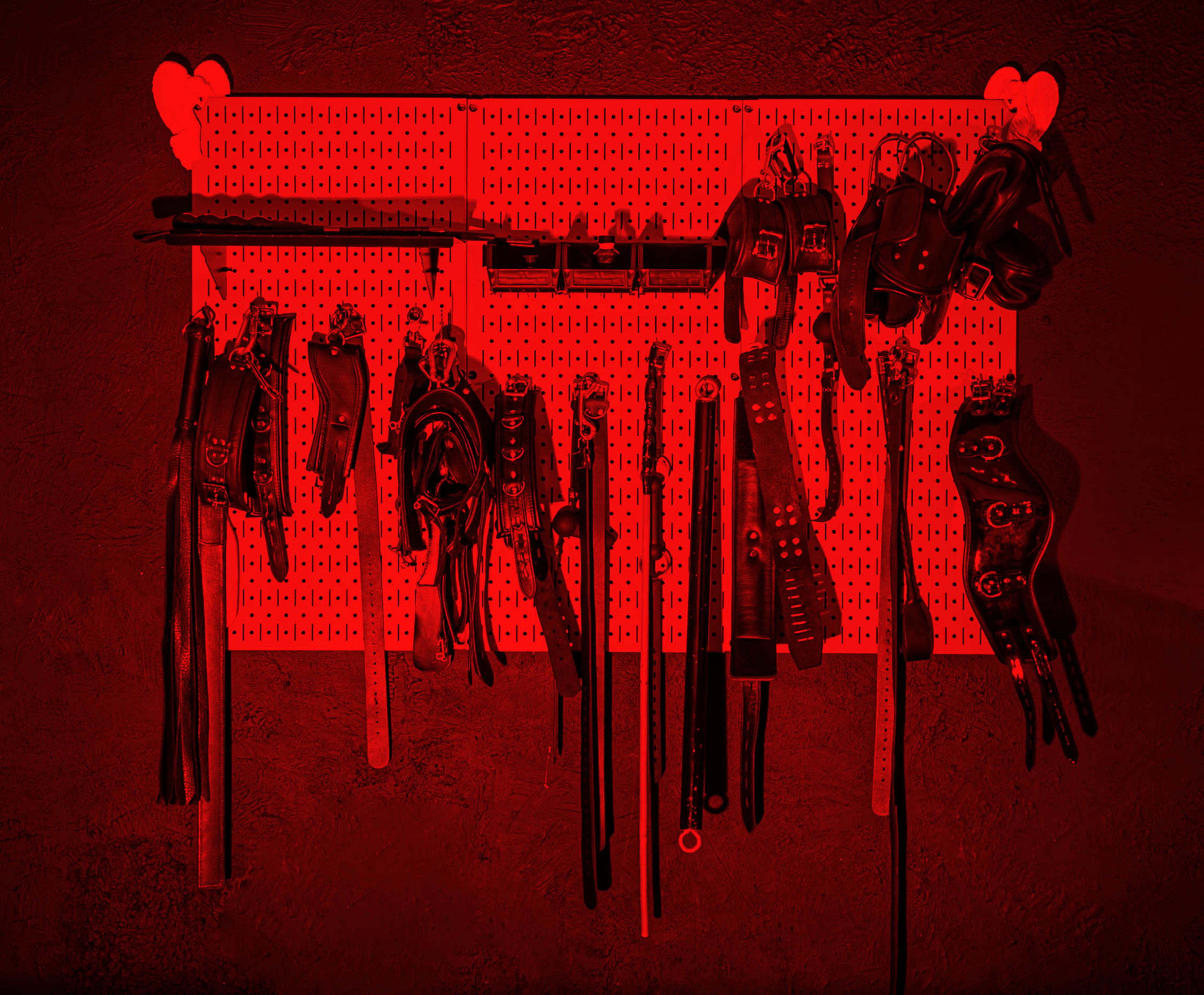 The image shows a pegboard displaying various leather straps, whips, and other accessories used for bondage or BDSM.