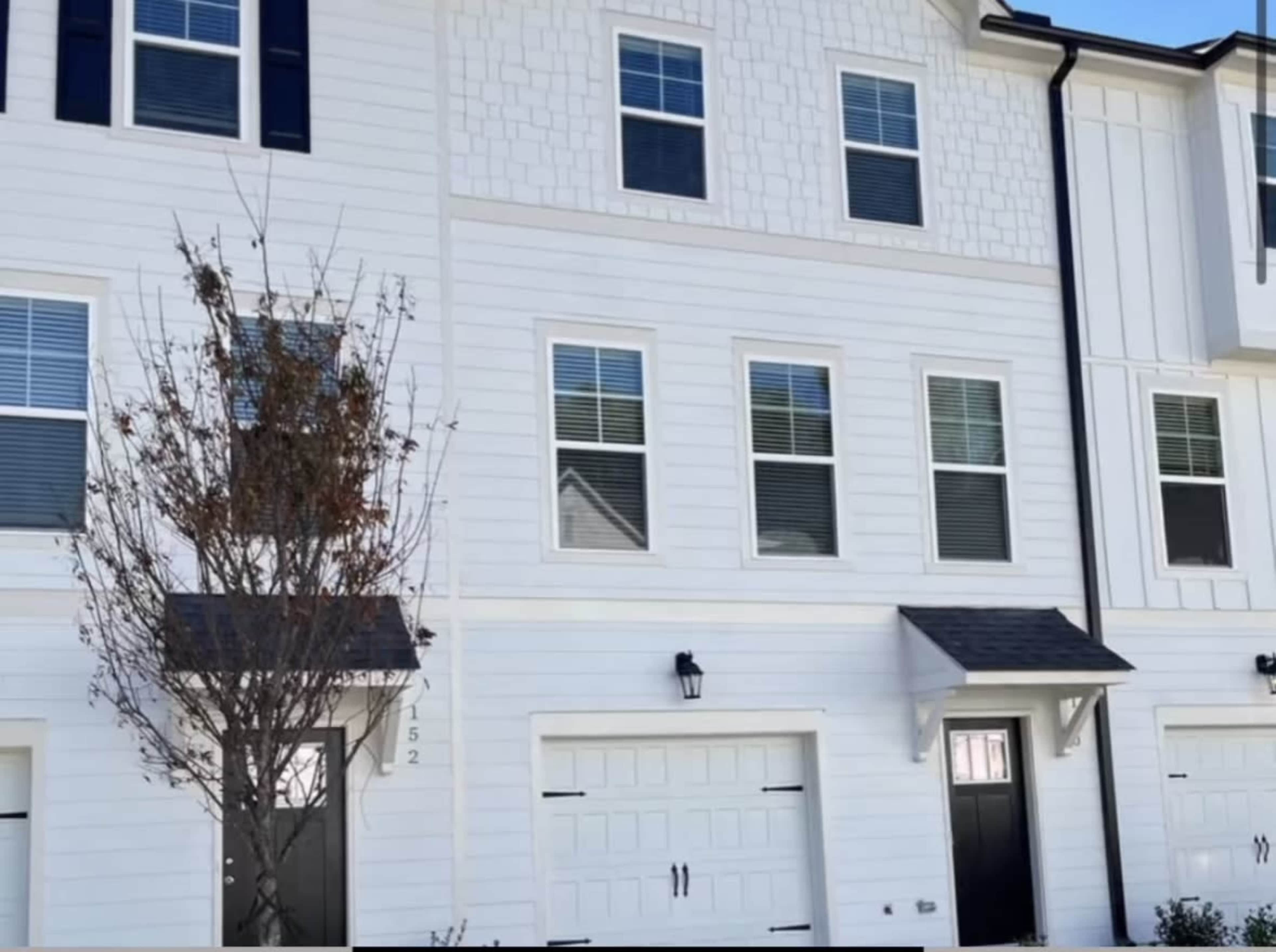 The image shows a row of modern townhouses with white siding, multiple windows, and a garage on the ground floor.