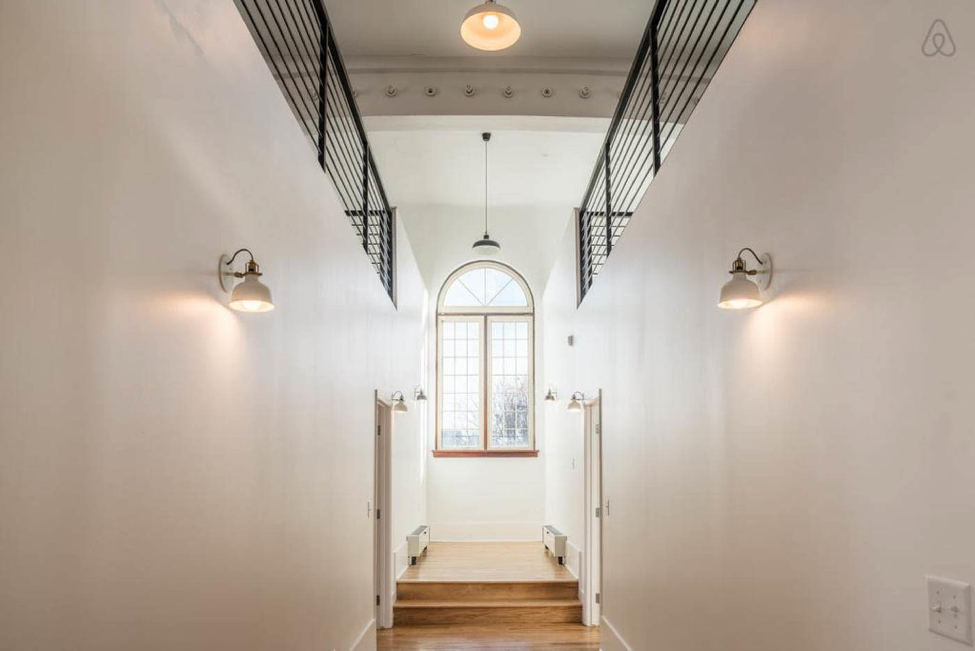 A long, bright hallway with a large arched window at one end, featuring wooden flooring and two doors on each side.