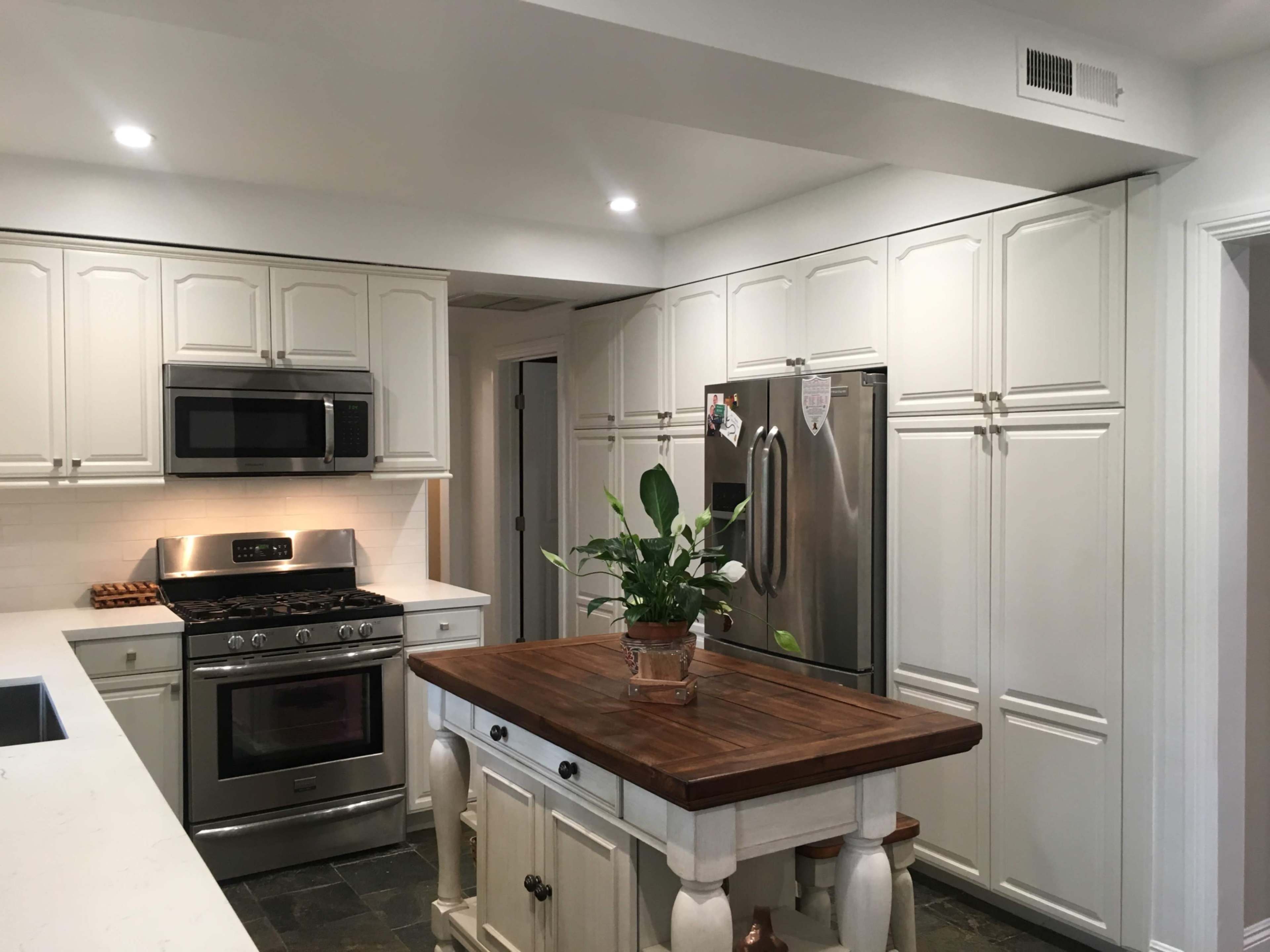 A modern kitchen features white cabinetry, stainless steel appliances, and a central wooden island with a plant on top.