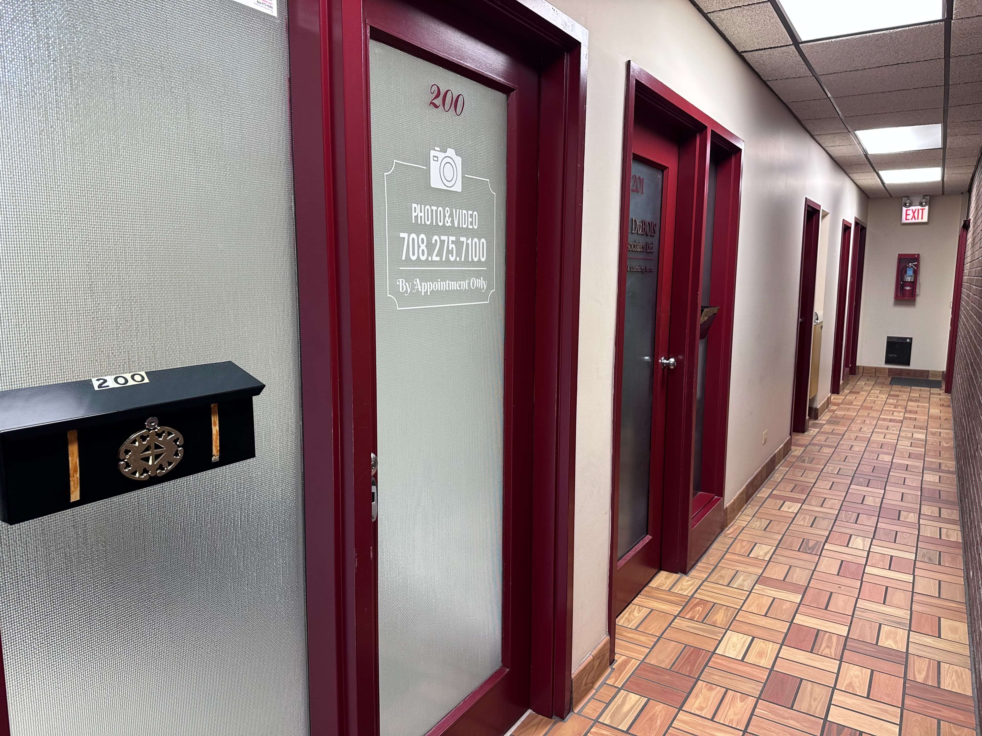 A hallway with multiple doors, including one marked "200," and a mailbox attached to the wall next to it, featuring the text "Photo & Video 708.275.7120 By Appointment Only."